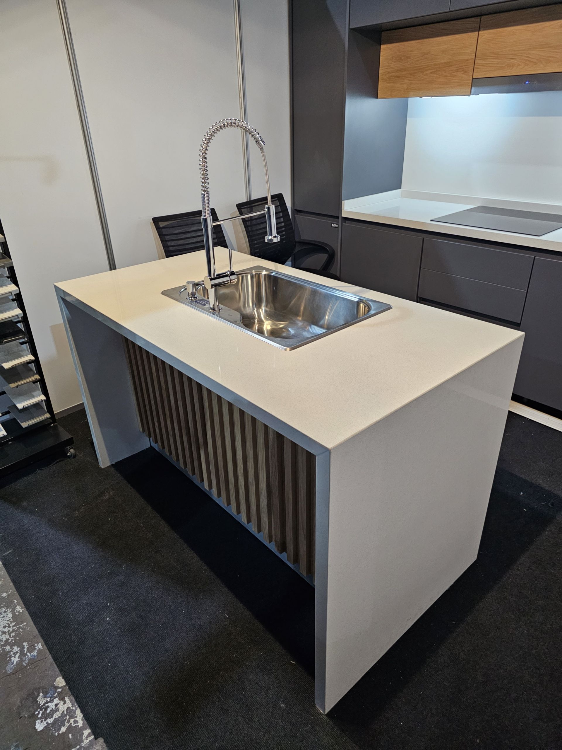 Isla de cocina moderna con fregadero de acero inoxidable, paneles de madera y encimera blanca.