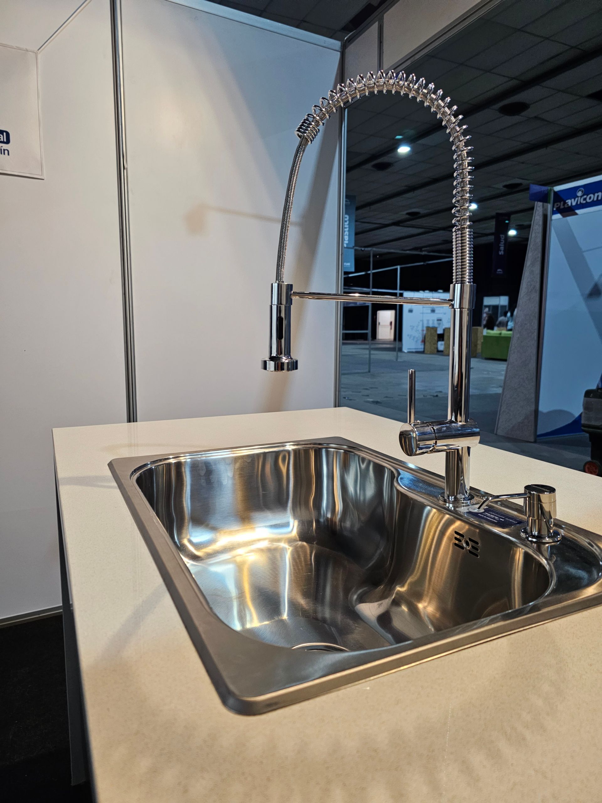 Fregadero de acero inoxidable con grifo de cuello de cisne cromado sobre encimera blanca.