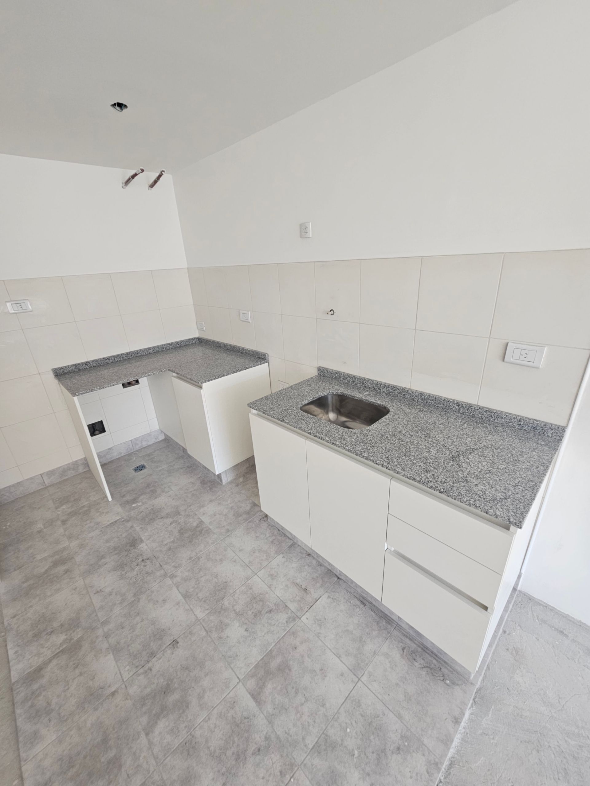 Gabinetes de cocina blancos con encimeras grises y fregadero.