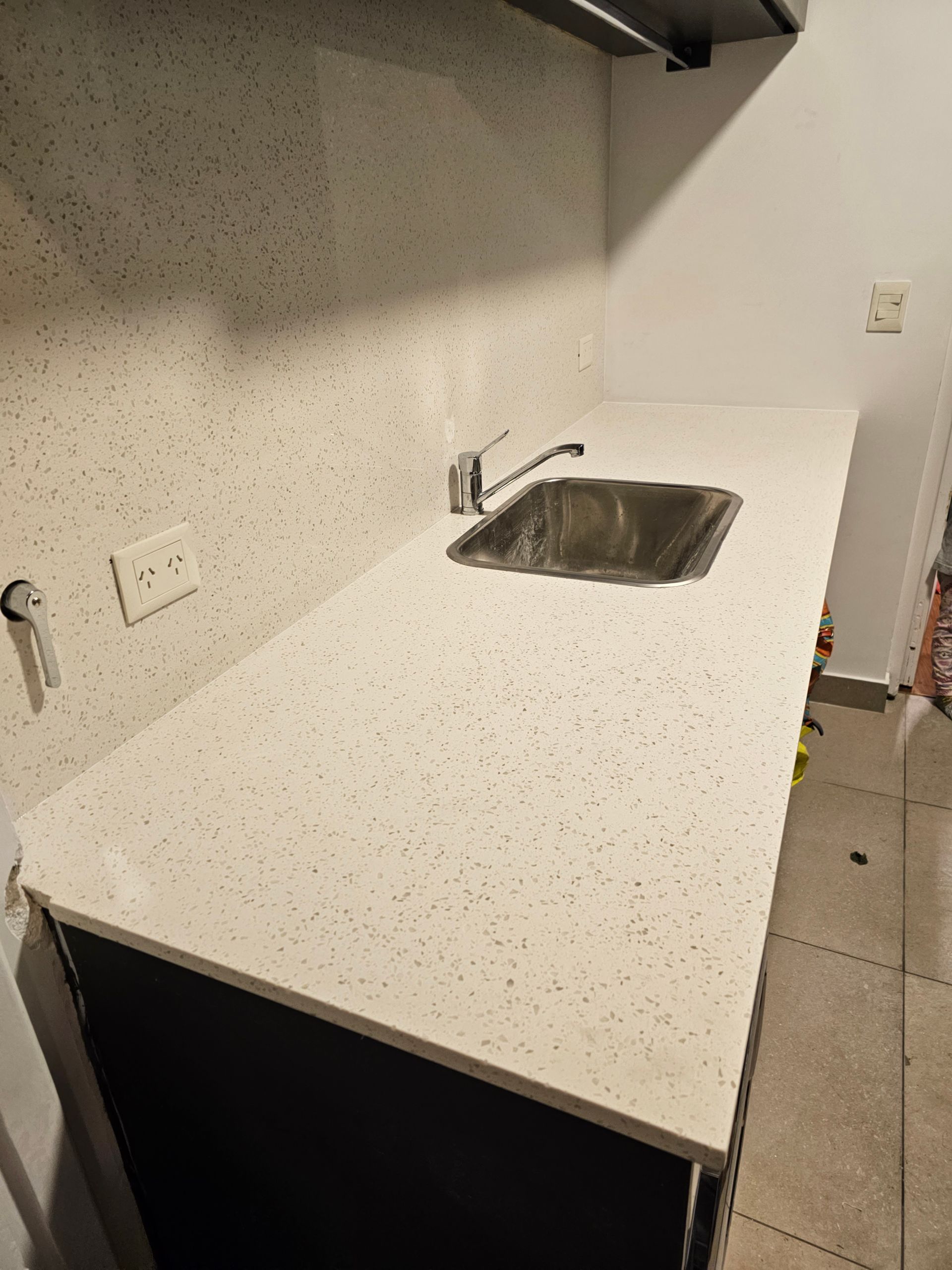 Una encimera de cocina con fregadero y grifo. Encimera blanca moteada, gabinetes oscuros.