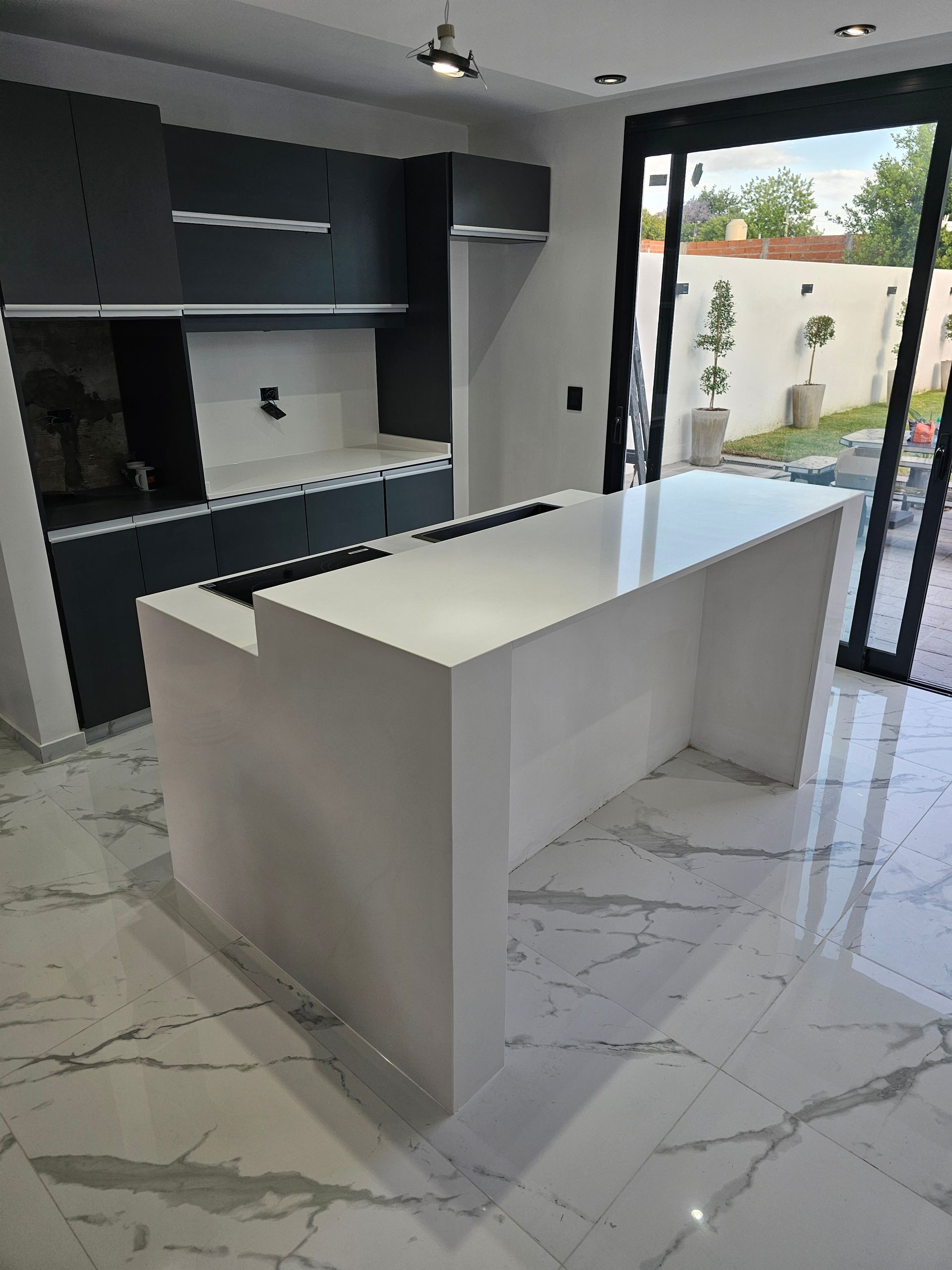 Cocina blanca moderna con isla, gabinetes oscuros y ventana grande con vista a un patio.