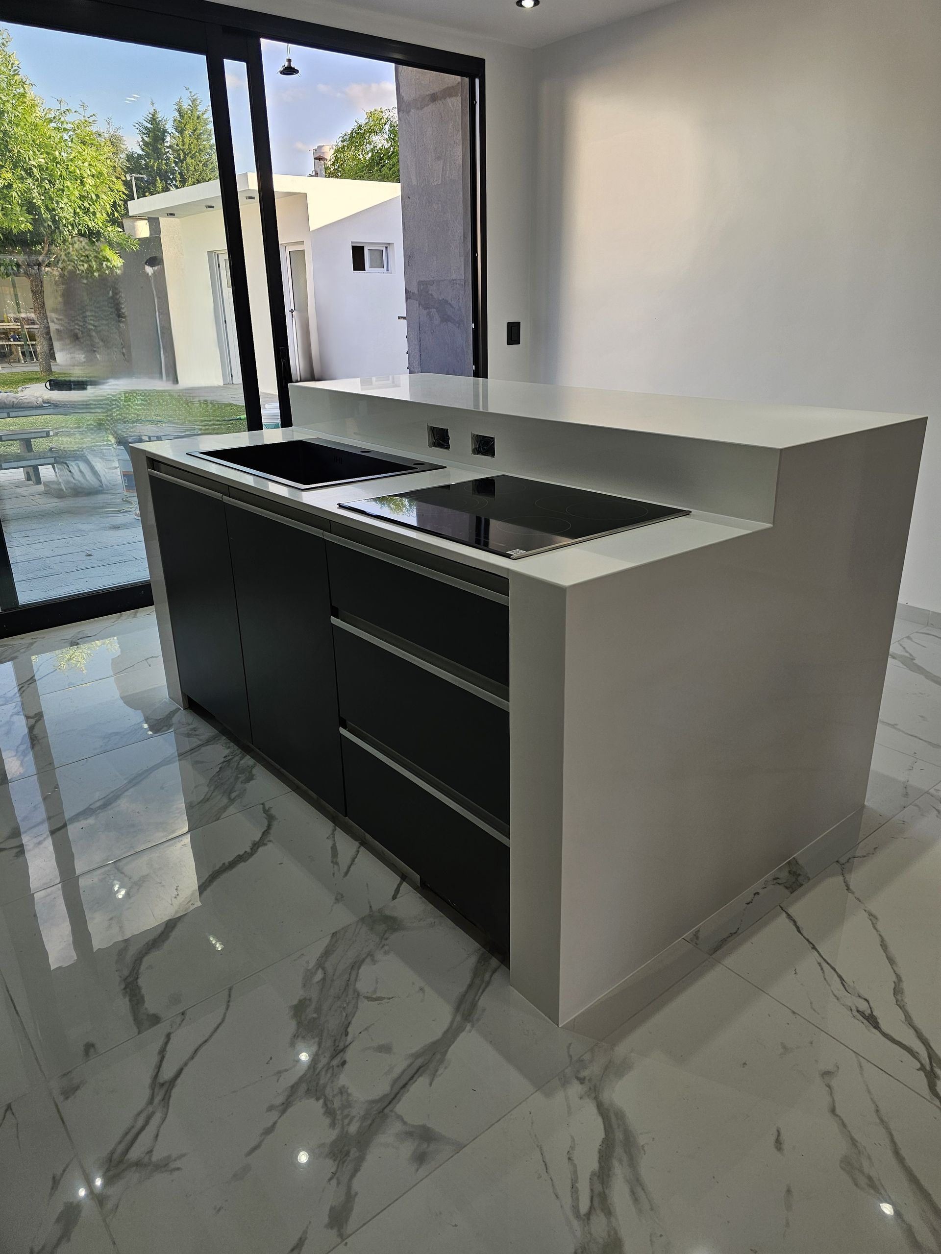 Isla de cocina moderna con gabinetes negros, encimera blanca y dos lavabos.