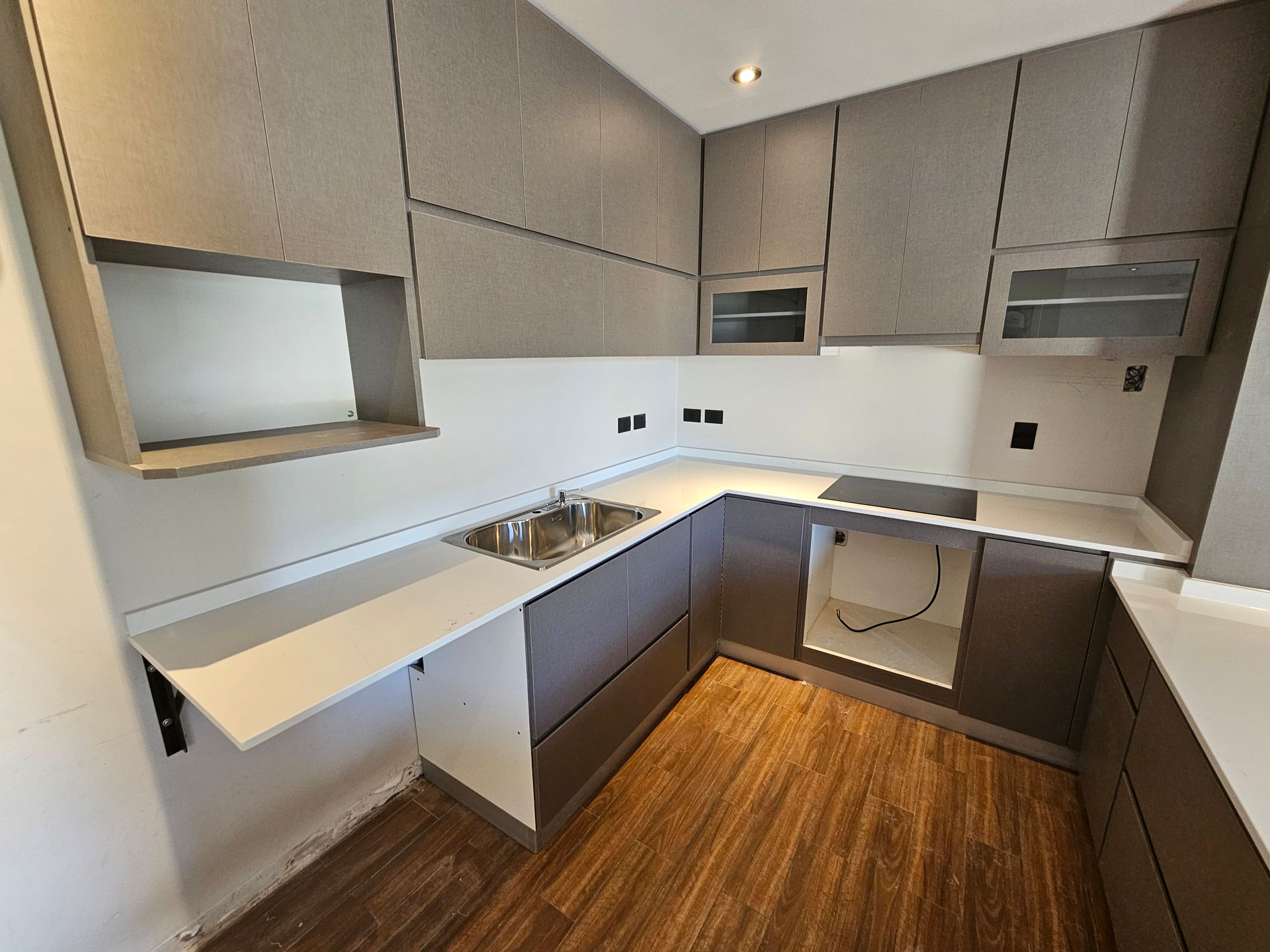 Cocina moderna con gabinetes grises, encimeras blancas y pisos con apariencia de madera.