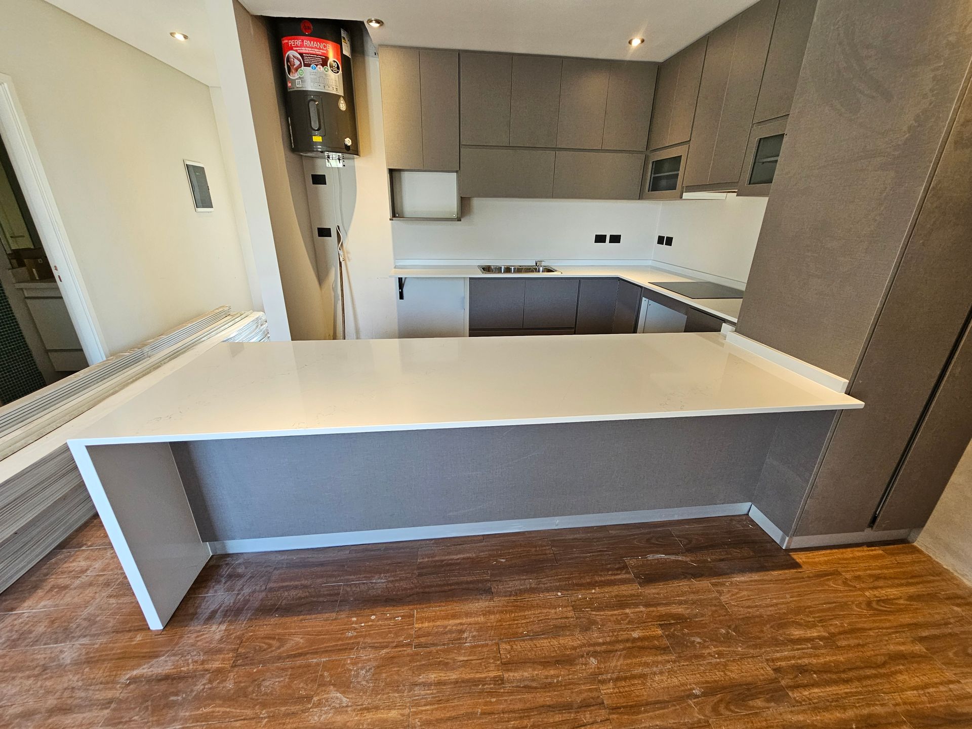 Cocina moderna con isla de encimera blanca, gabinetes grises y pisos con apariencia de madera.