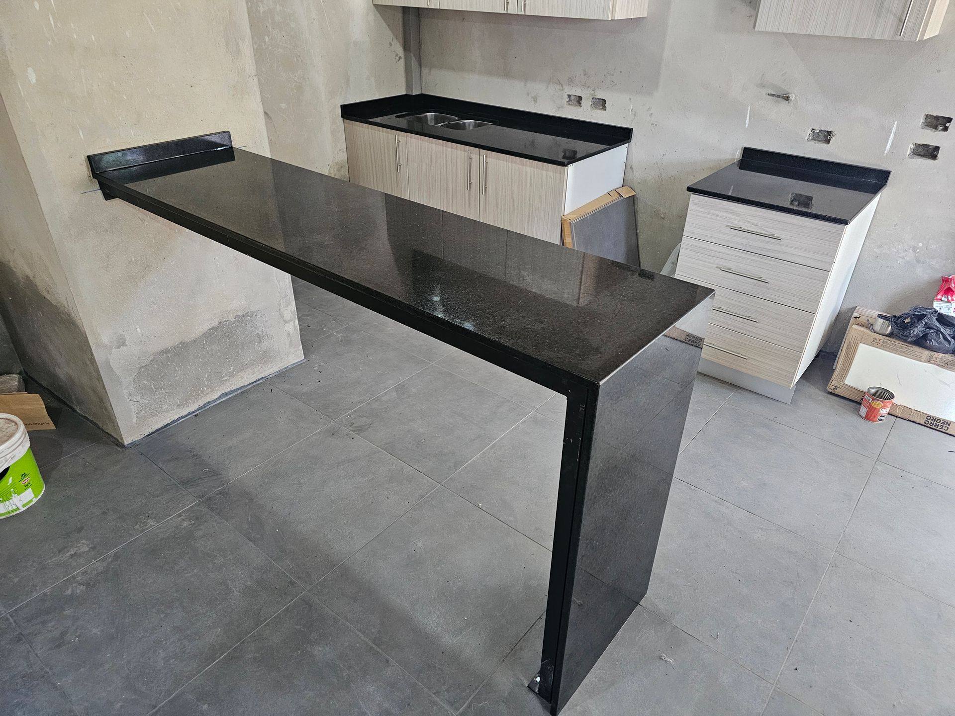 Encimera de granito negro que sobresale de la pared, formando una barra. Cocina en construcción sin terminar.