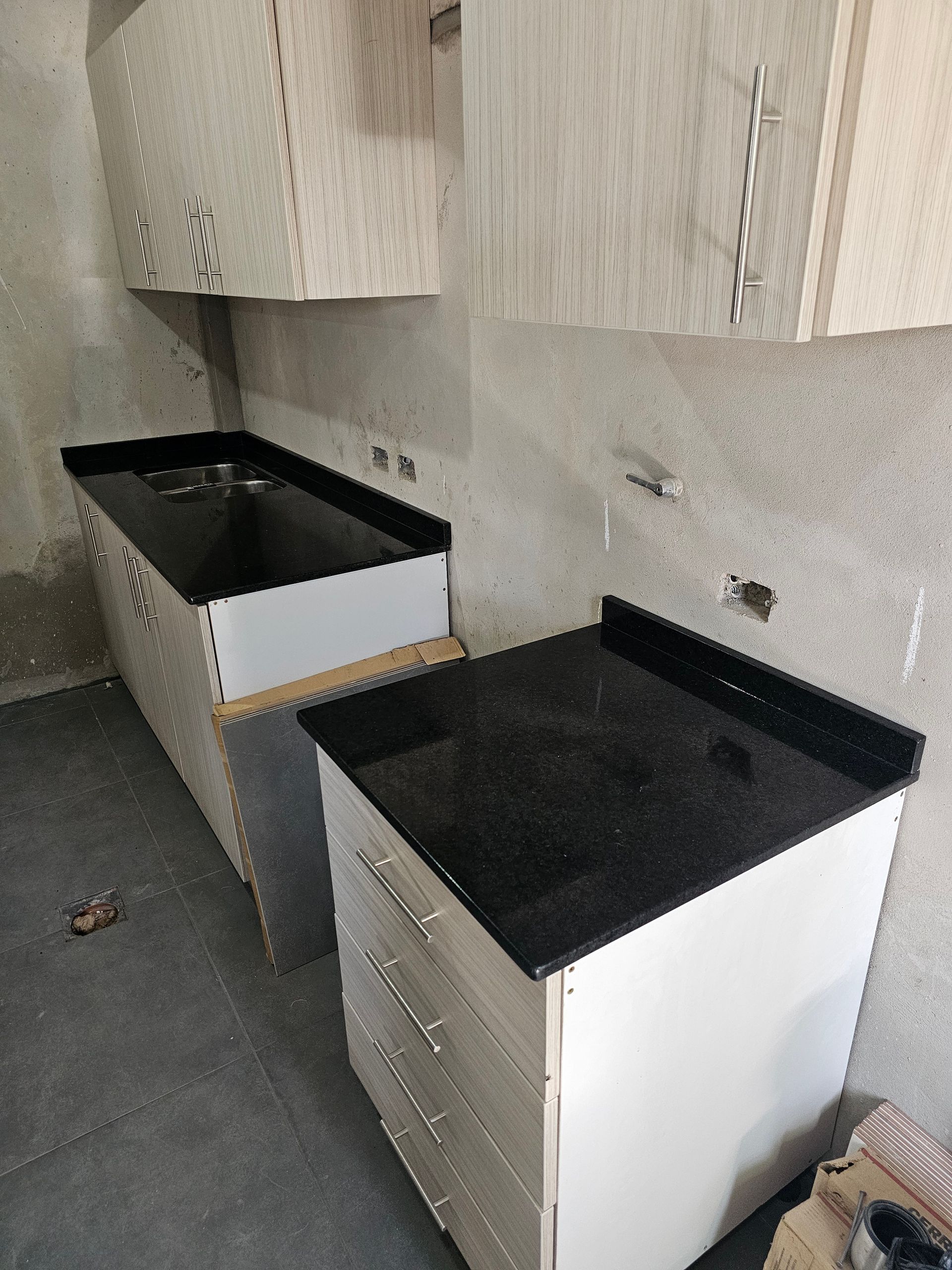 Muebles de cocina con encimeras en color negro, instalados en una habitación en construcción.