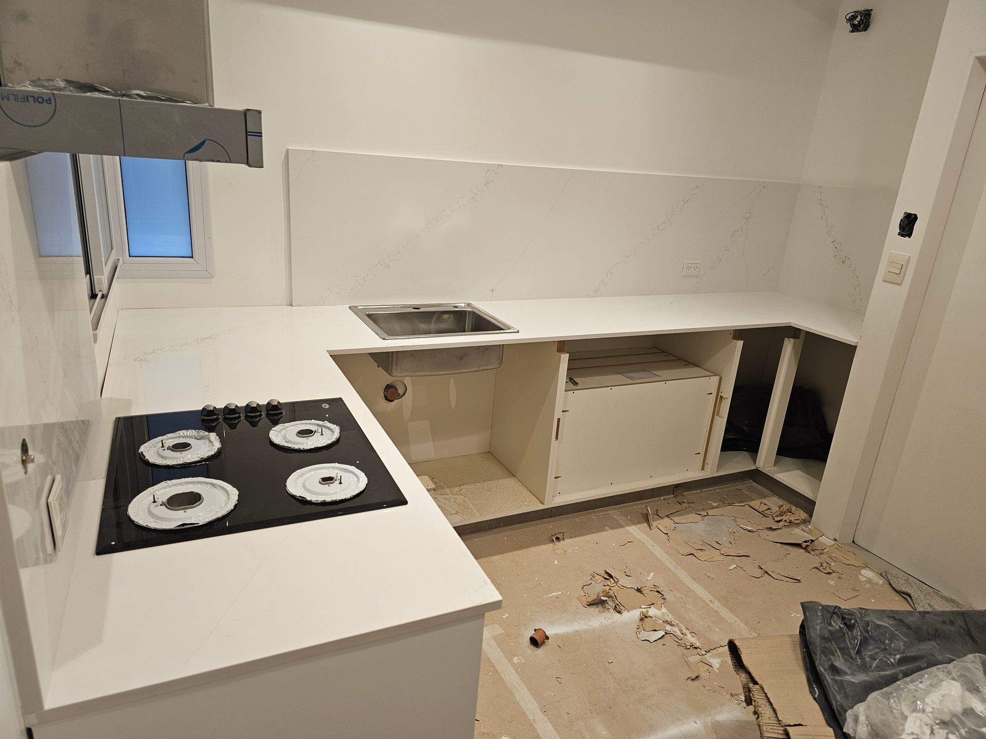 Cocina en construcción con encimeras blancas, anafe y fregadero.