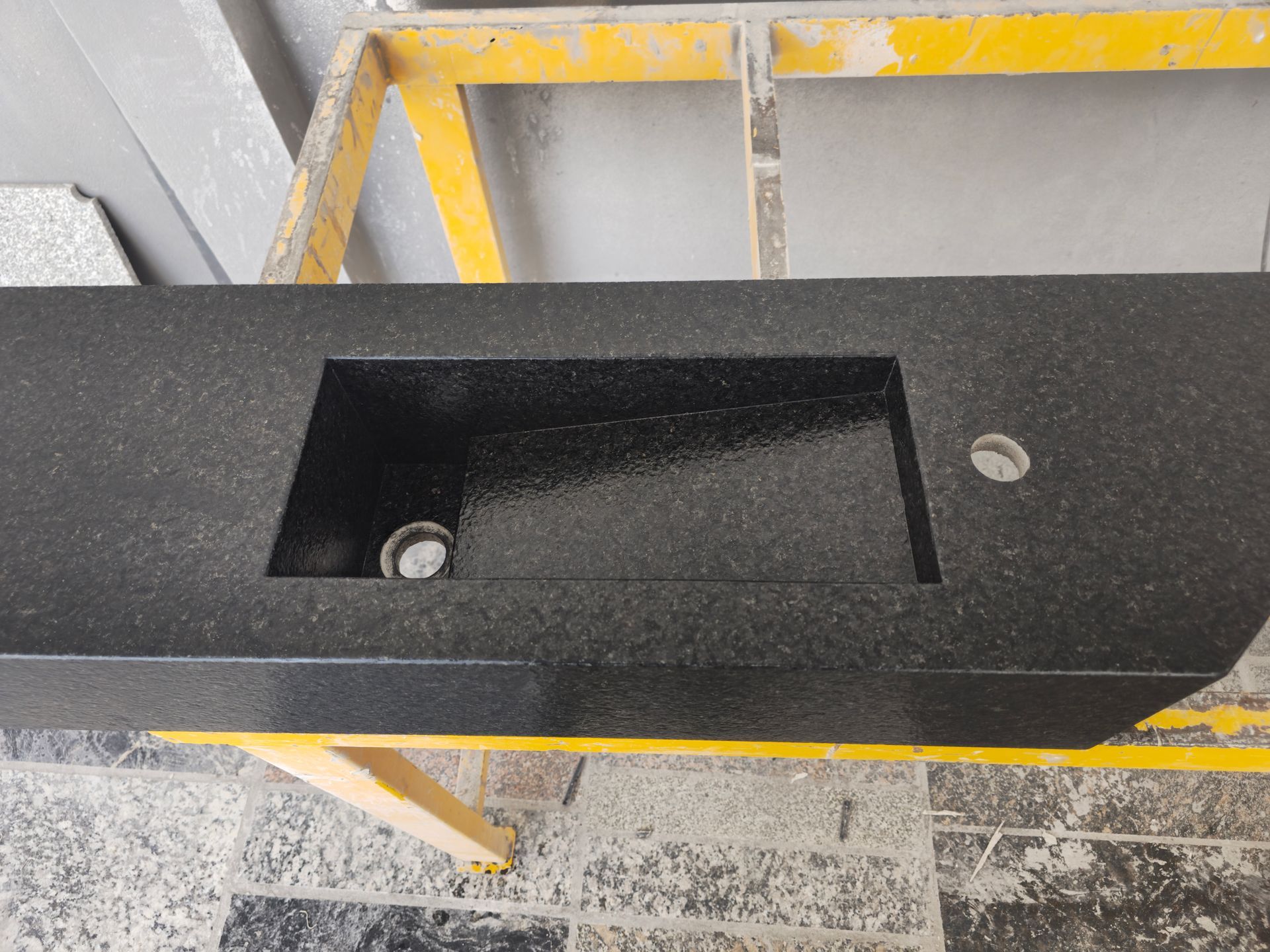 Encimera de granito negro con fregadero rectangular incorporado y orificio para grifo, sobre caballete amarillo.