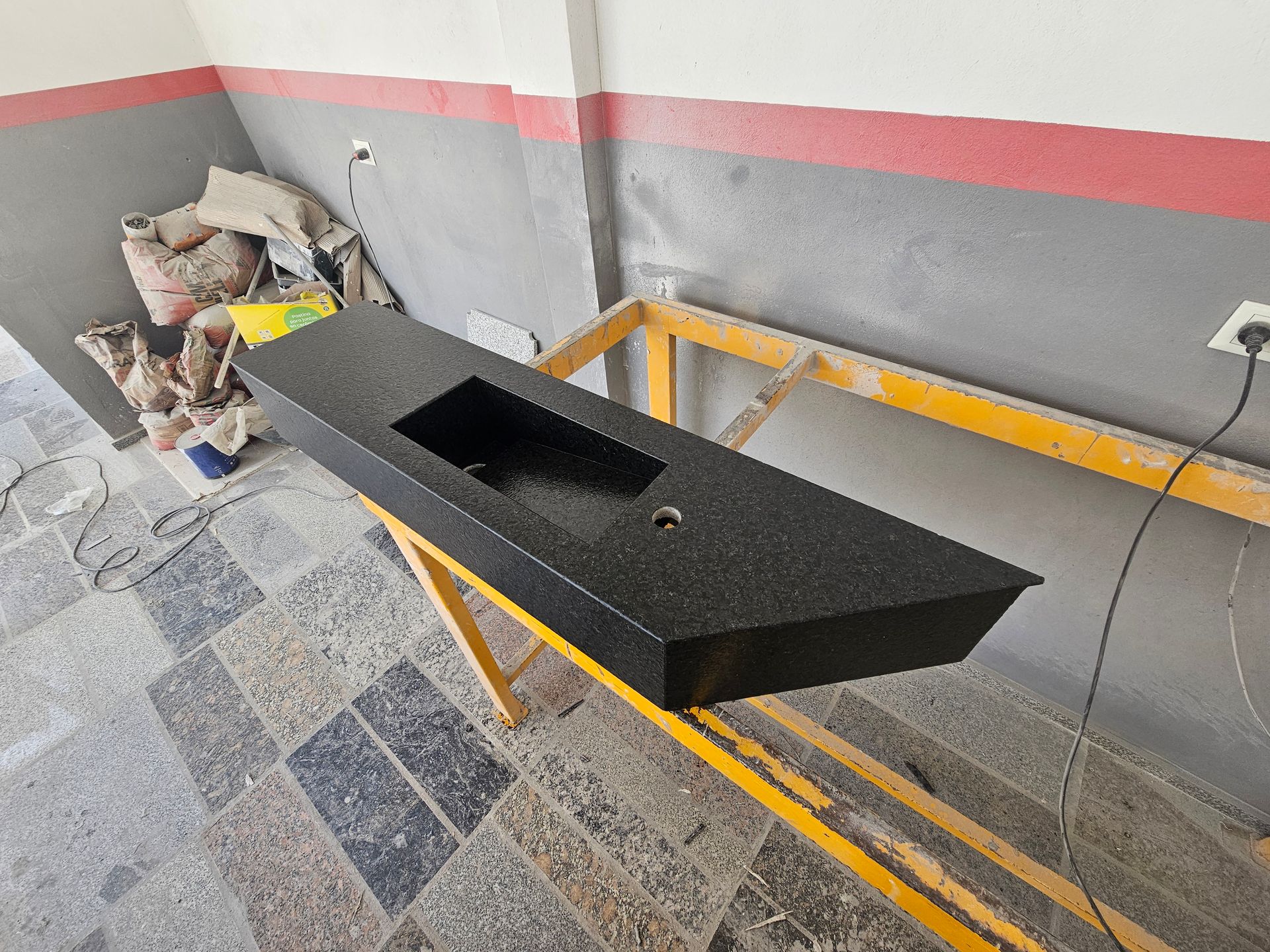 Encimera negra con fregadero incorporado sobre soporte amarillo, en entorno de taller.