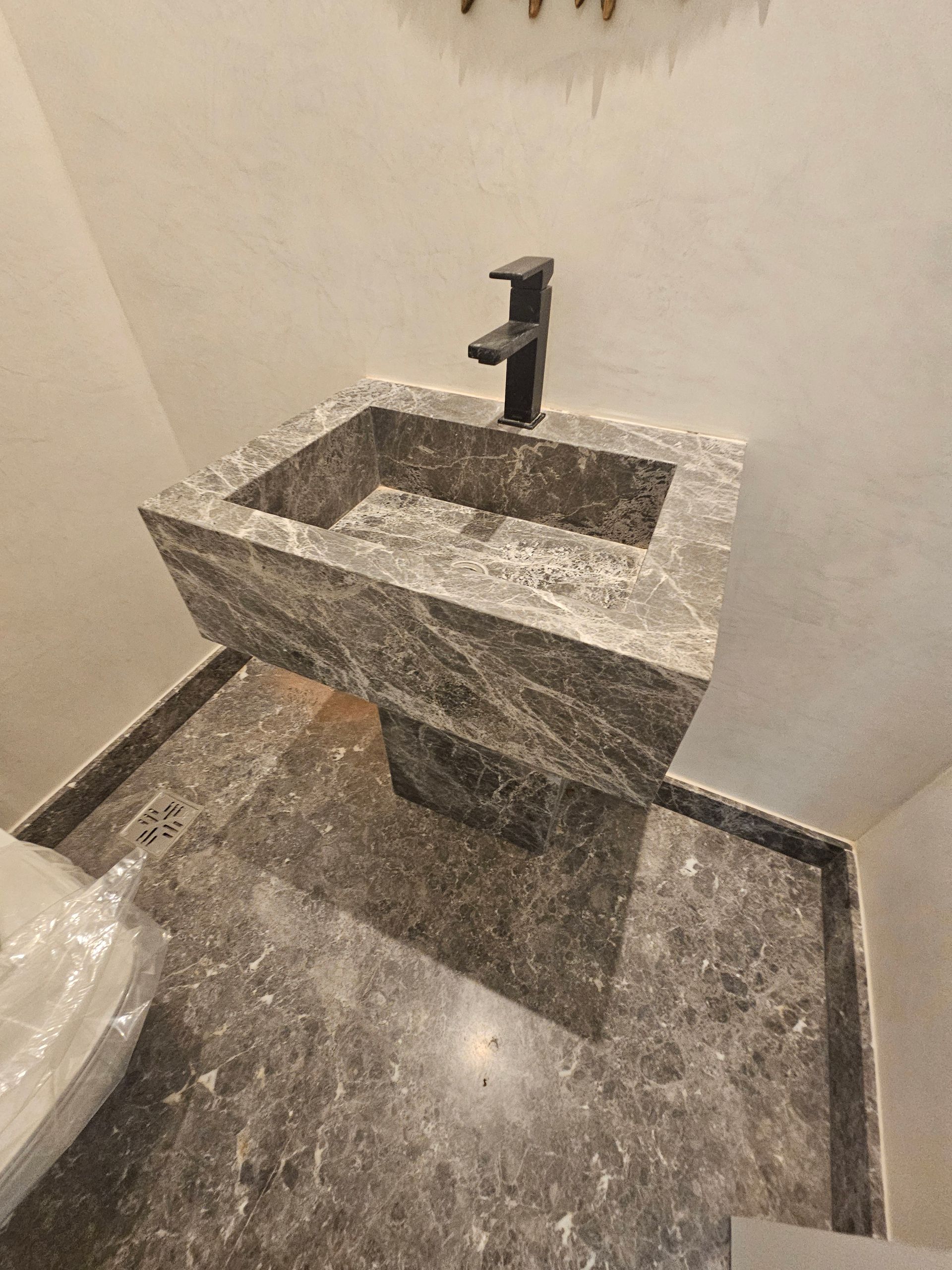 Lavabo con pedestal de mármol gris con grifo negro en un baño.
