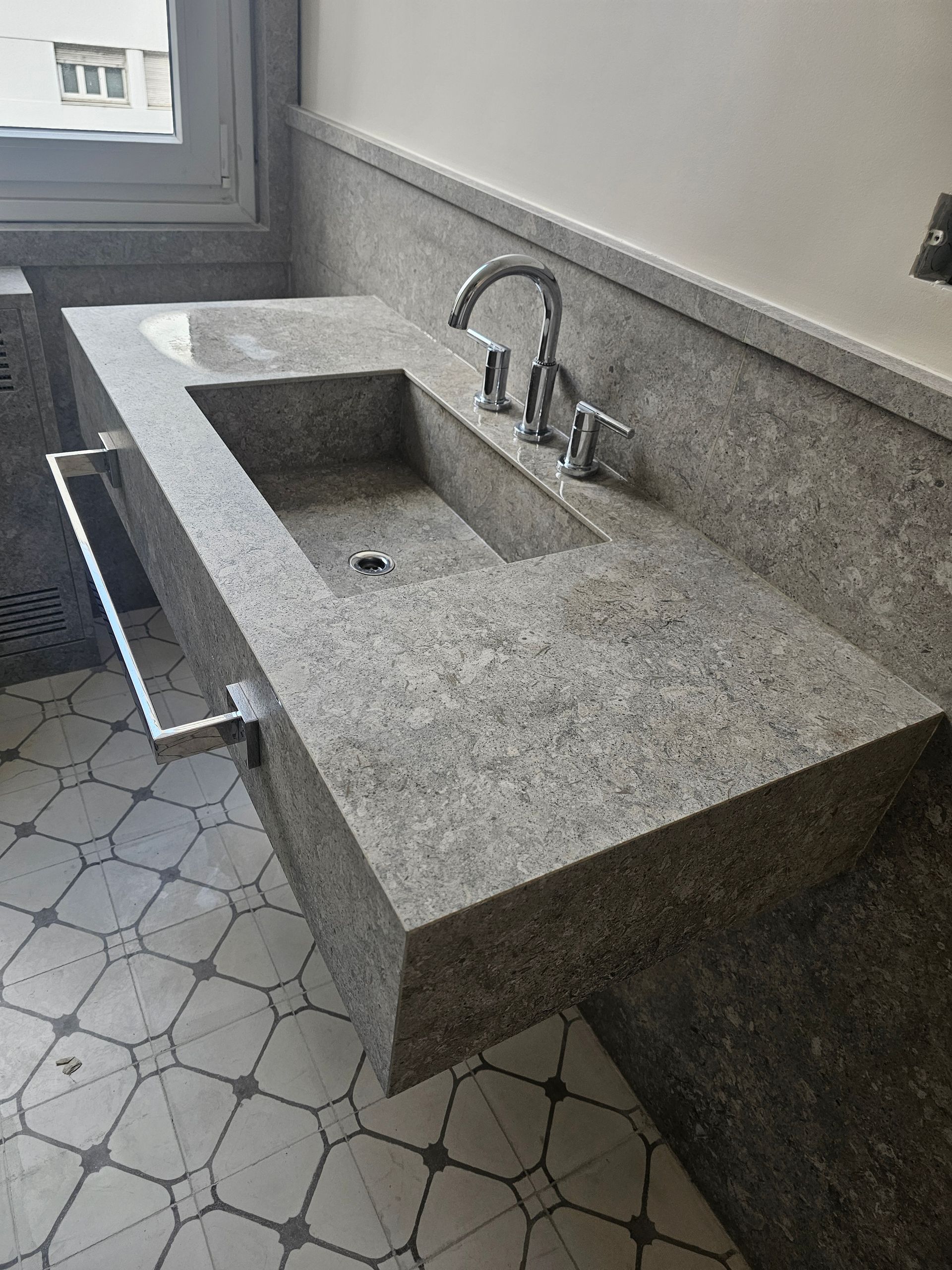 Tocador de baño de granito gris con lavabo rectangular incorporado, grifo cromado y toallero.