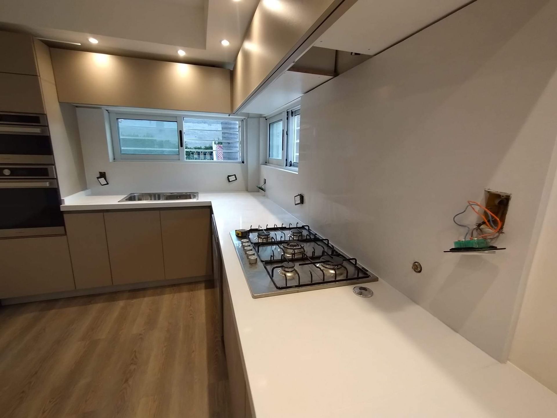 Cocina moderna con gabinetes de colores claros, encimeras y estufa a gas de acero inoxidable cerca de una ventana.