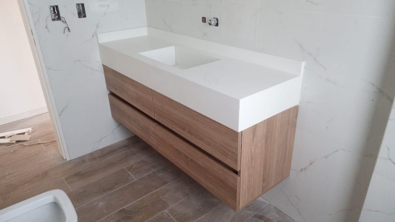 Mueble de baño flotante con cajones de madera clara y encimera blanca con lavabo.
