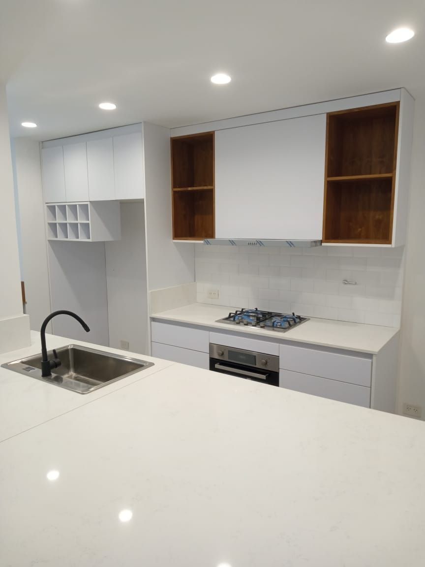 Cocina blanca moderna con detalles de madera, que incluye fregadero, estufa y gabinetes superiores.