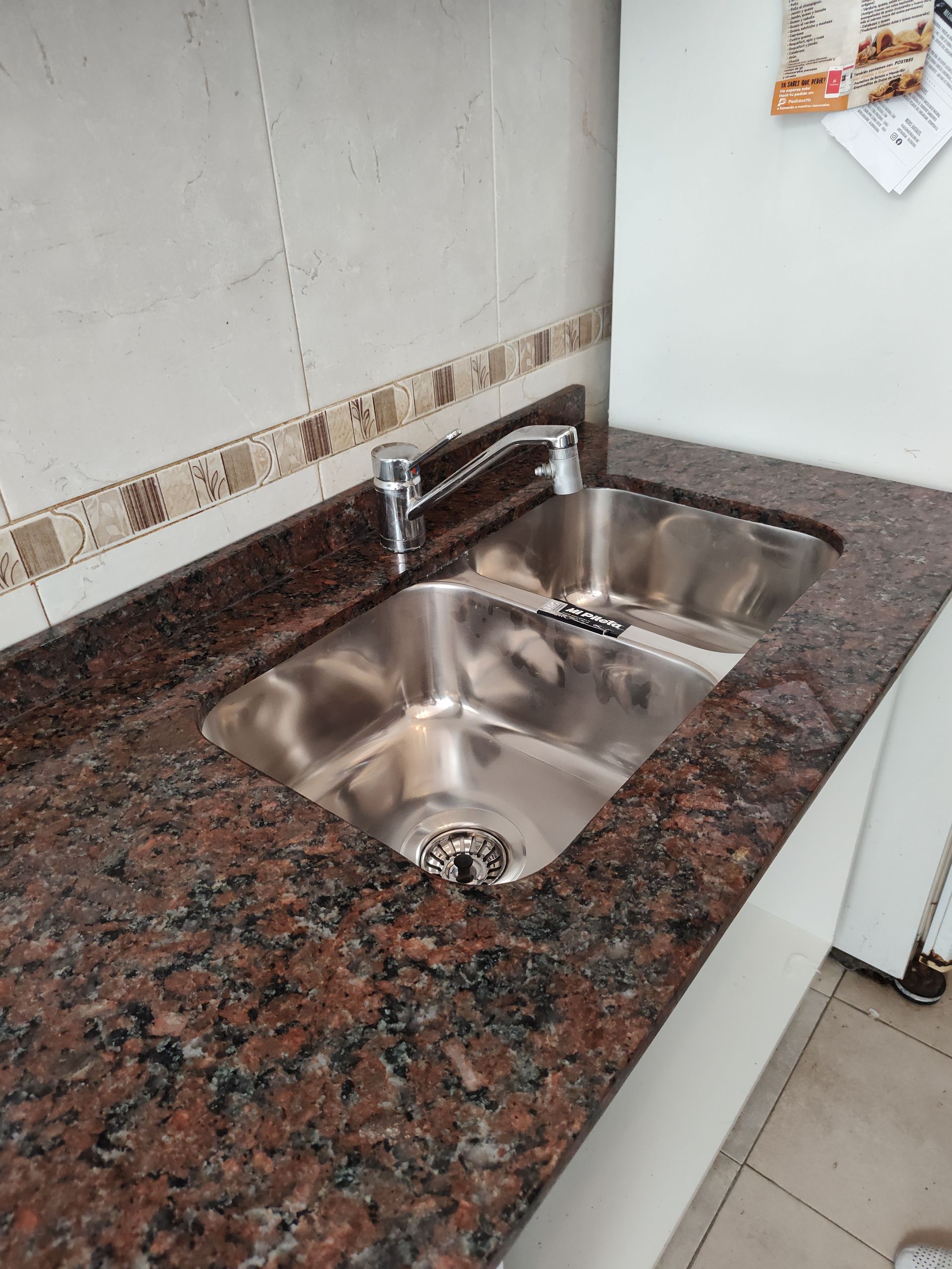 Fregadero de cocina doble de acero inoxidable con encimera de granito marrón y grifo cromado.