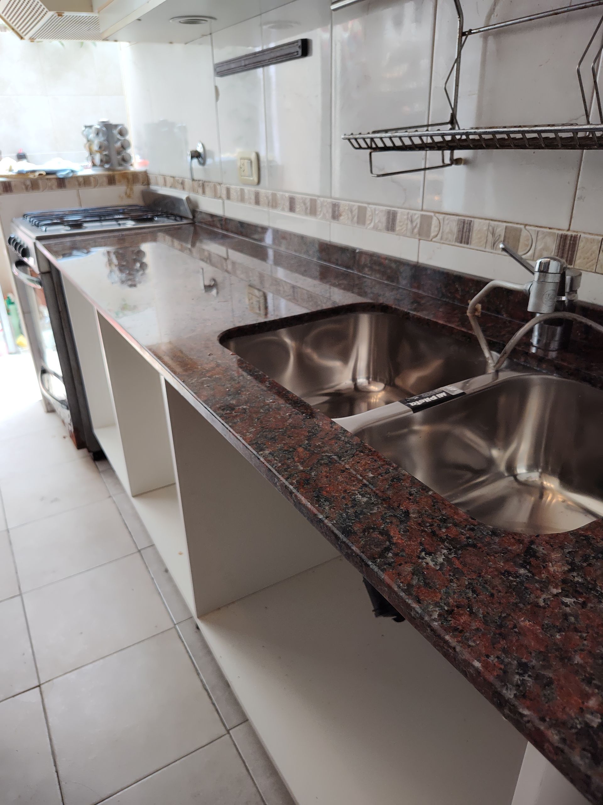 Cocina con encimera de granito marrón rojizo y fregadero de acero inoxidable.