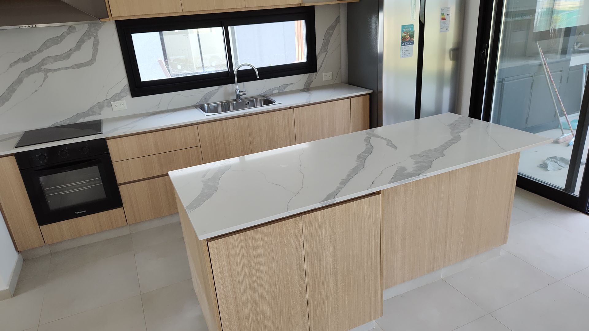 Cocina moderna con gabinetes de madera clara, encimeras de mármol blanco y una isla central.