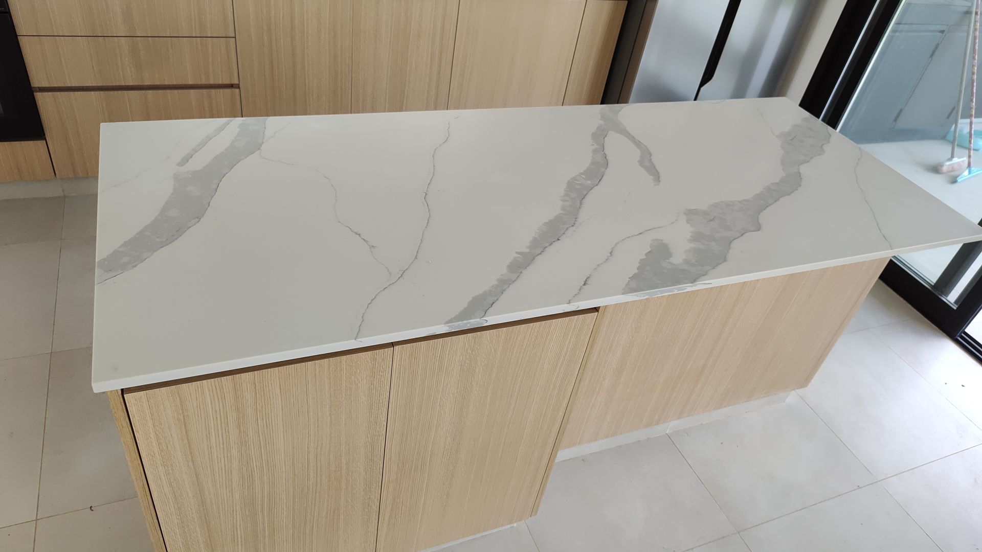 Una isla de cocina de roble claro con una encimera de cuarzo blanco con vetas grises.