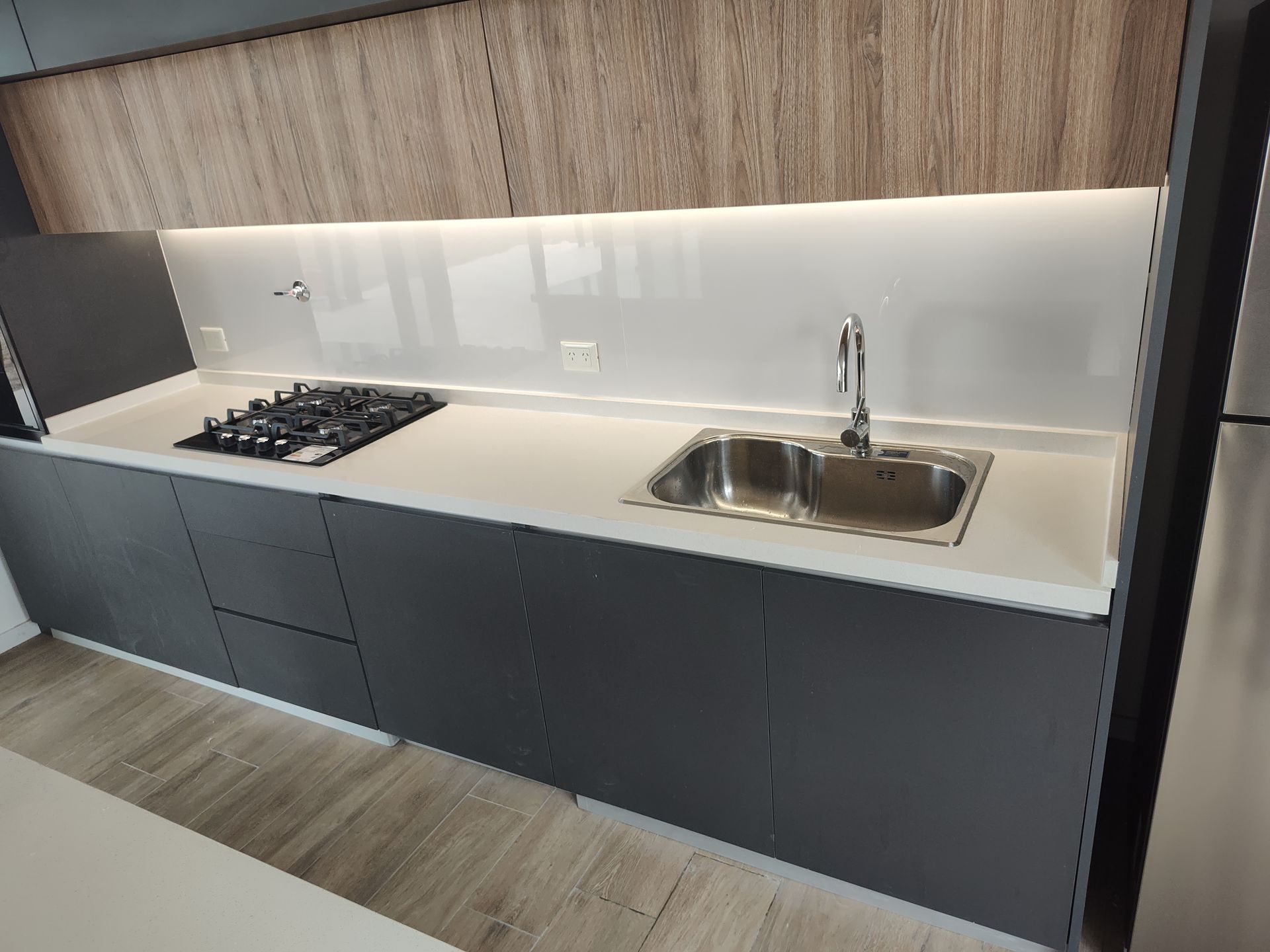 Cocina moderna con gabinetes grises, encimeras blancas y fregadero de acero inoxidable.