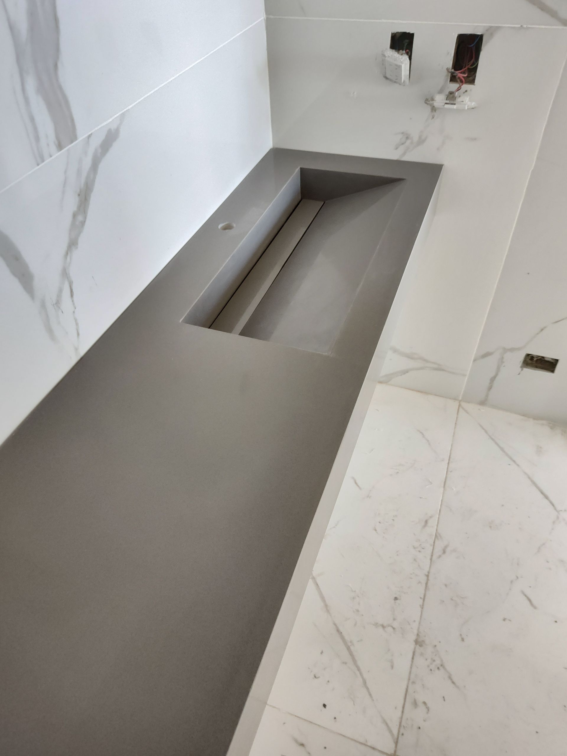 Lavabo y encimera empotrados de color gris. Azulejos de mármol blanco en paredes y suelo.