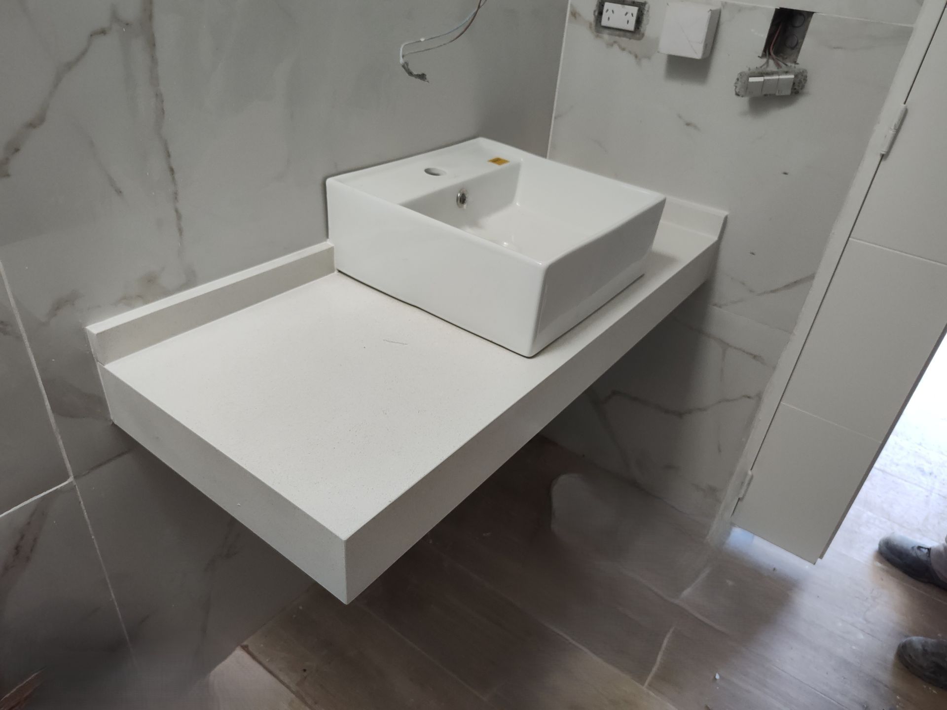 Mueble de baño flotante blanco con lavabo rectangular, instalado contra una pared con diseño de mármol.
