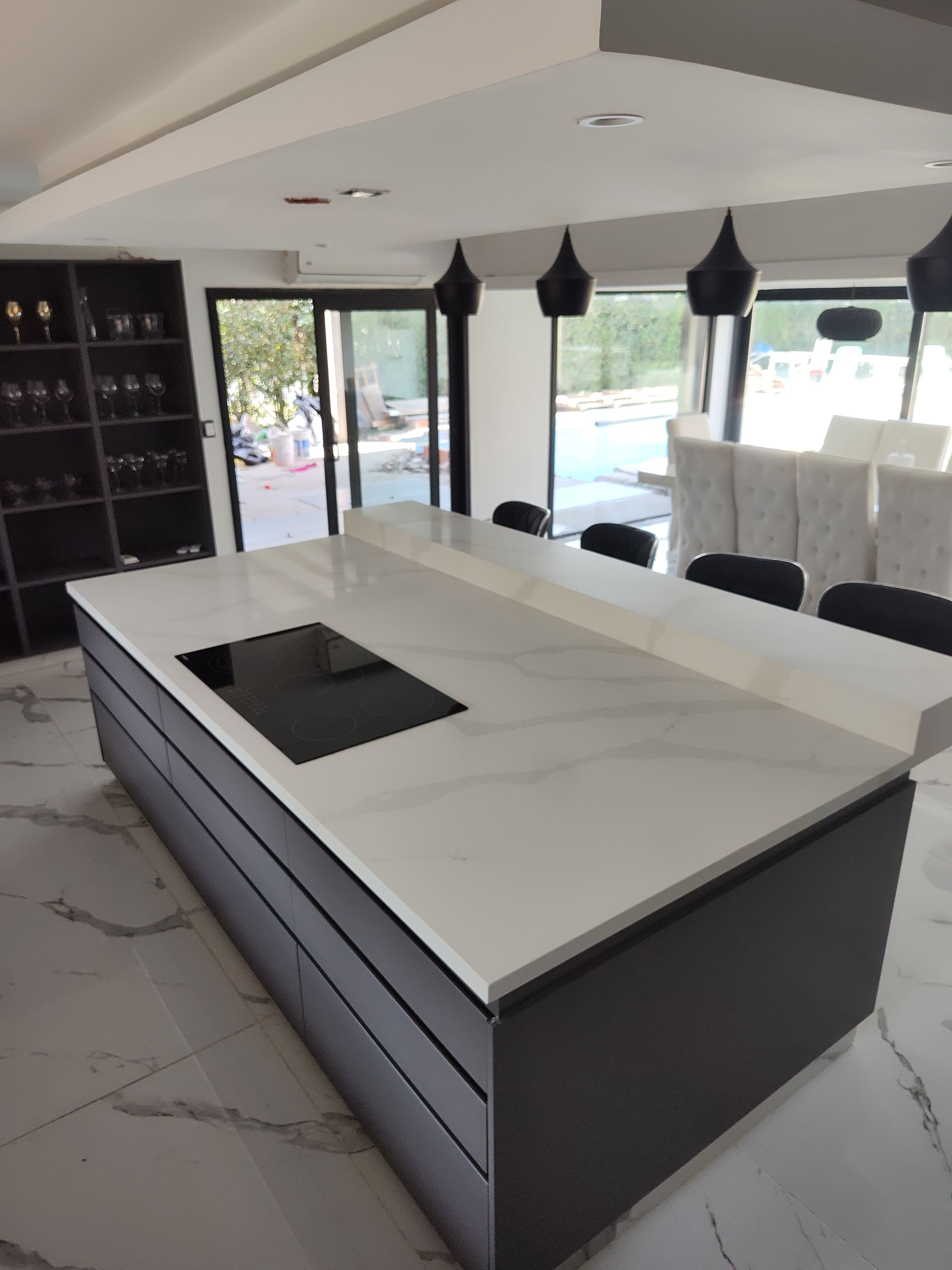 Cocina moderna con gabinetes oscuros, encimera blanca, isla con anafe y luces colgantes.