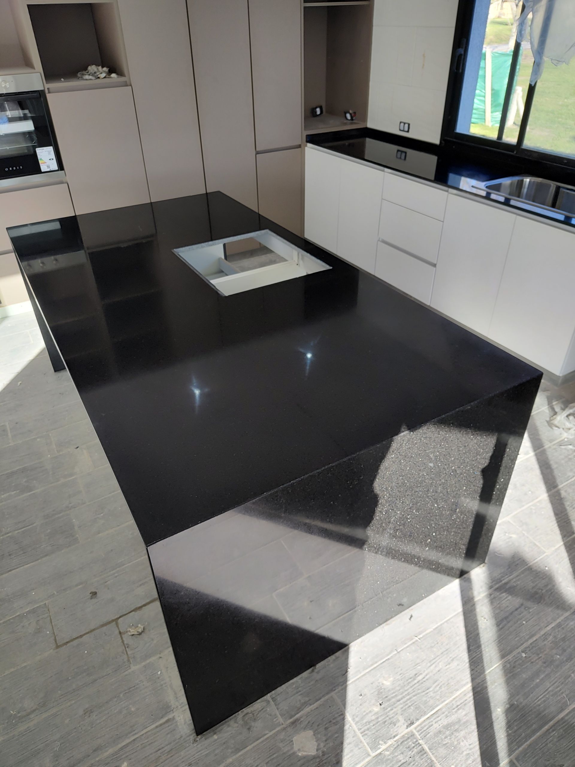 Isla de cocina negra con anafe incorporado, superficie reflectante, gabinetes blancos en el fondo.