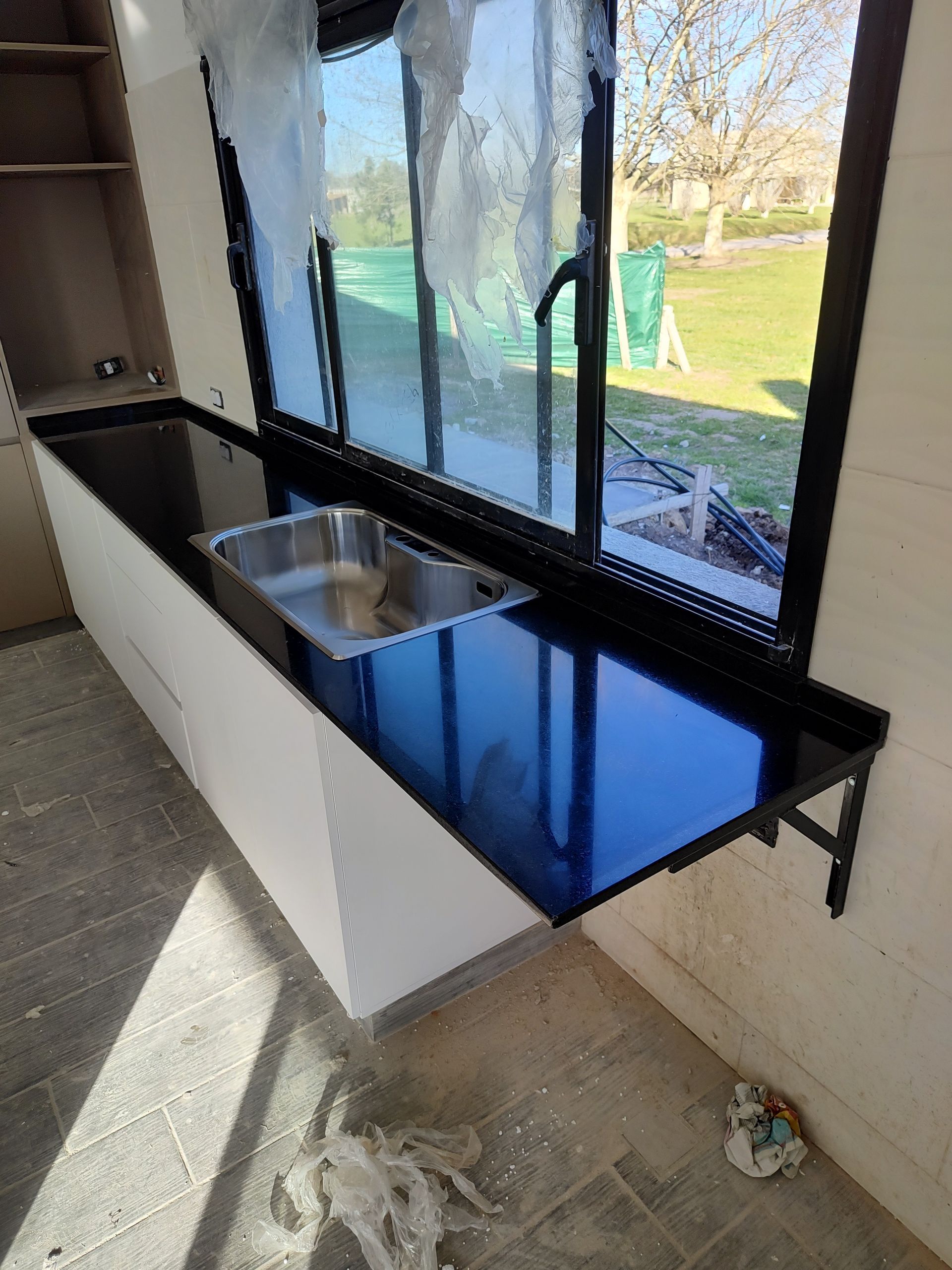 Cocina con encimera negra, fregadero de acero inoxidable y gabinetes blancos debajo de una ventana.