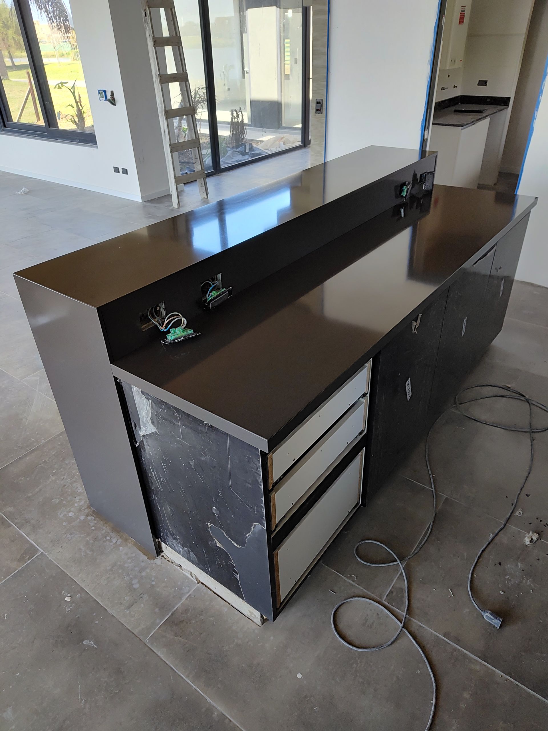 Isla de cocina gris oscuro con cajones, encimera negra y enchufes eléctricos.