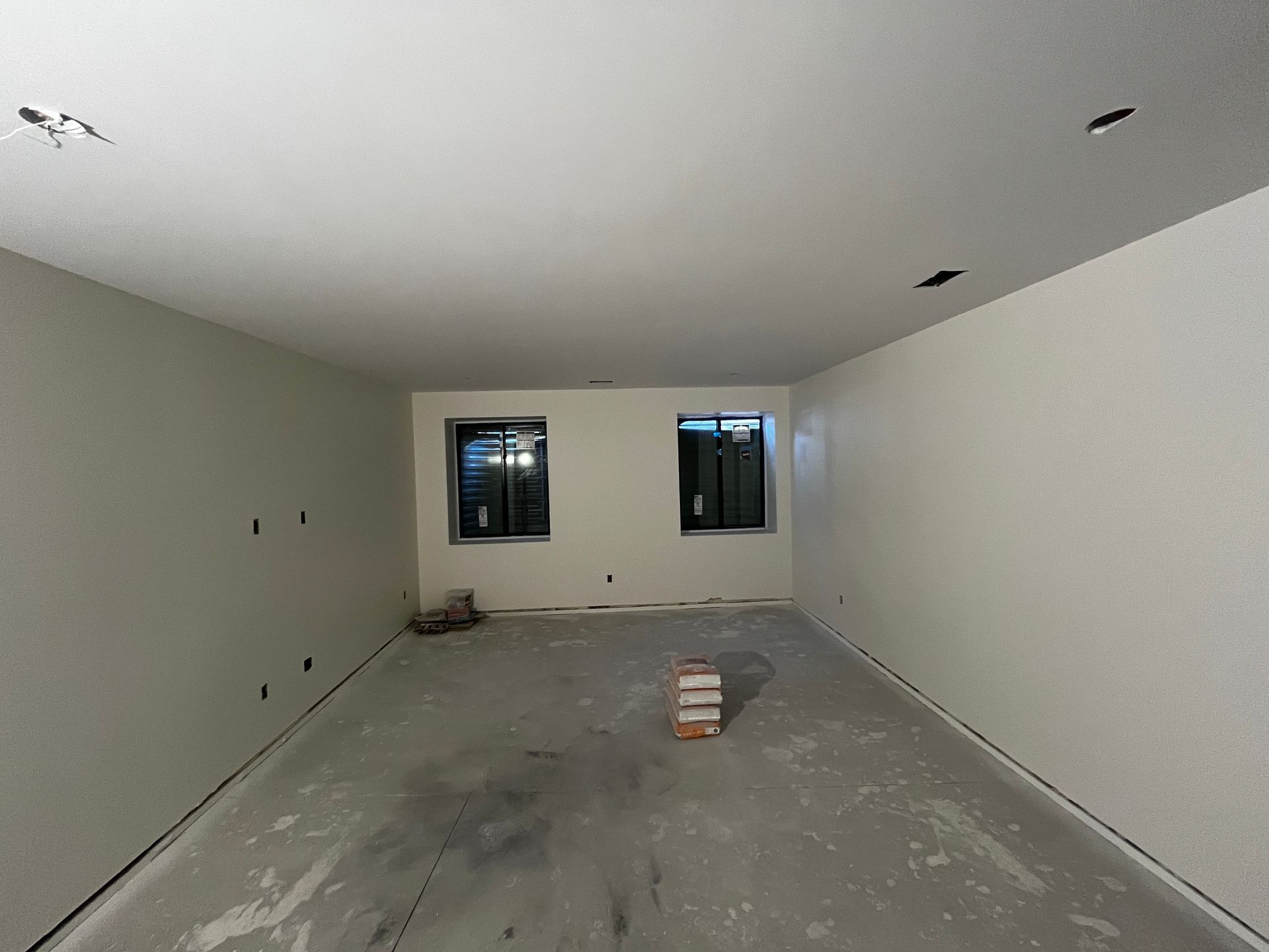 An empty room with two windows and a box on the floor.