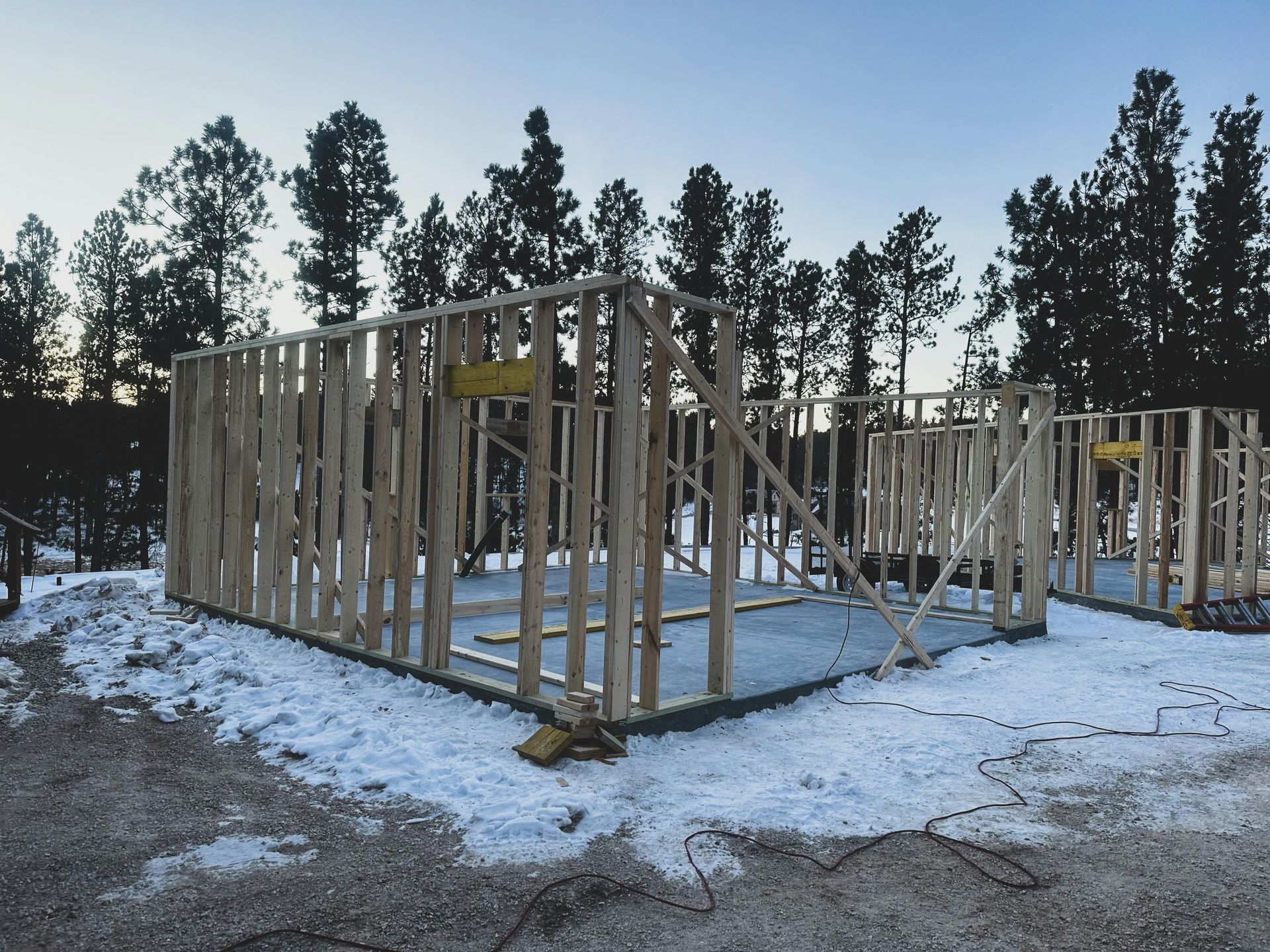 A house is being built in the snow with trees in the background.
