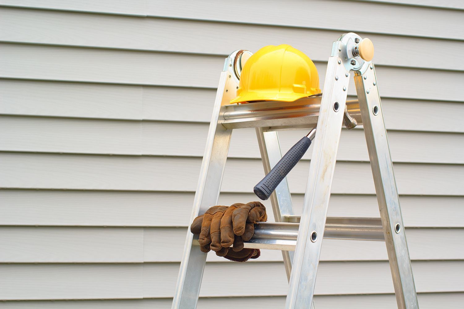 Construction tools and helmet on ladder prepared for siding repair project on modern home wall.