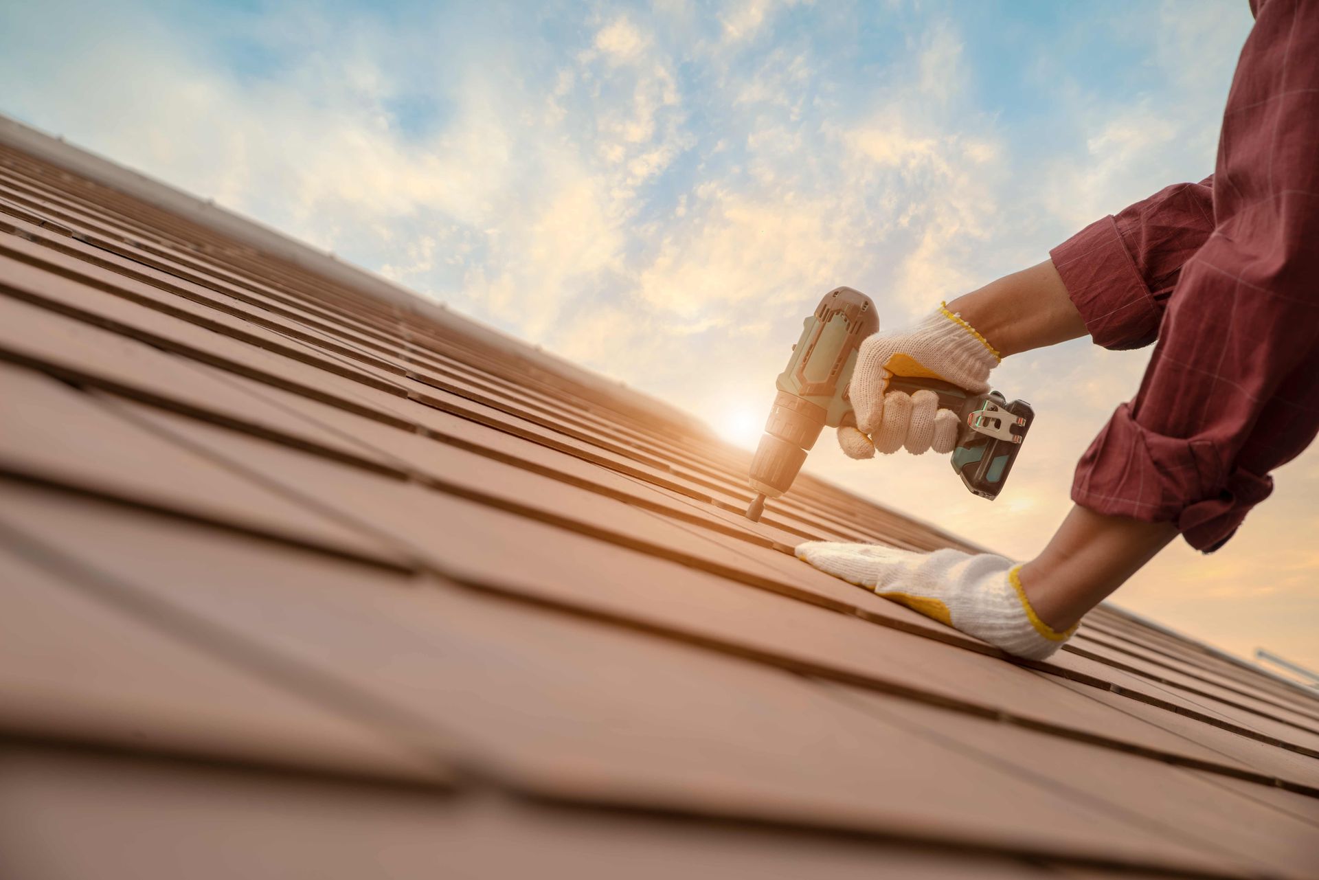 Man on roof at sunset, showcasing a roofing contractor’s skilled work and beautiful scenery.