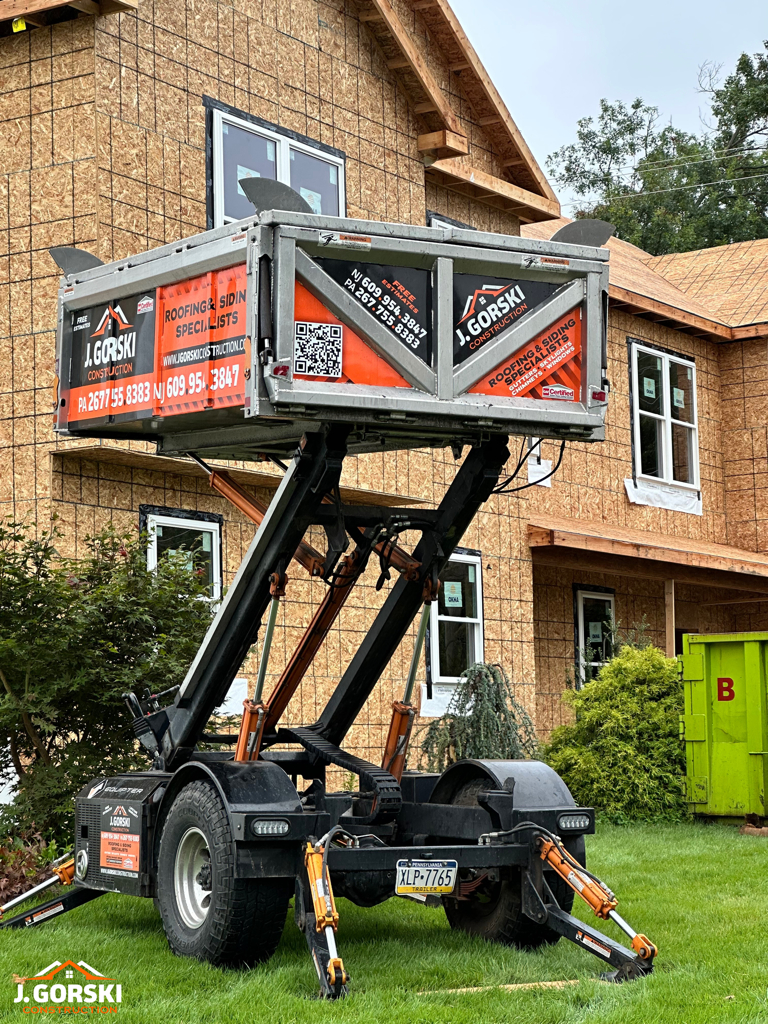 A trailer with a raised dumpster in front of a house under construction.