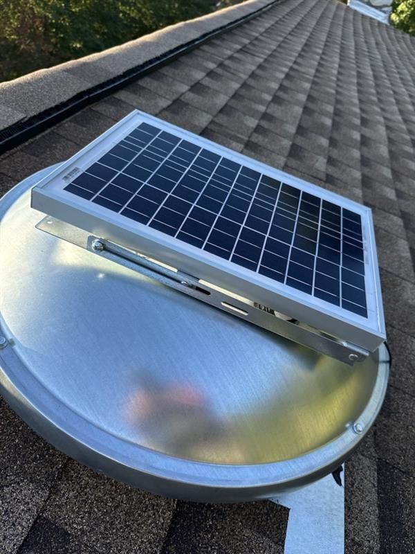 Solar-powered roof vent with solar panel mounted on a metal base against a brown shingle roof.