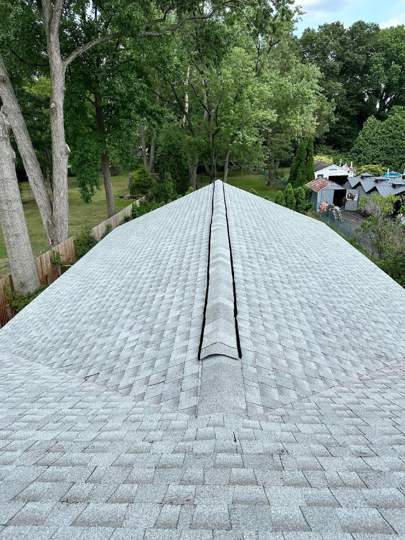 Overhead view of a gray asphalt shingle roof with trees in the background.