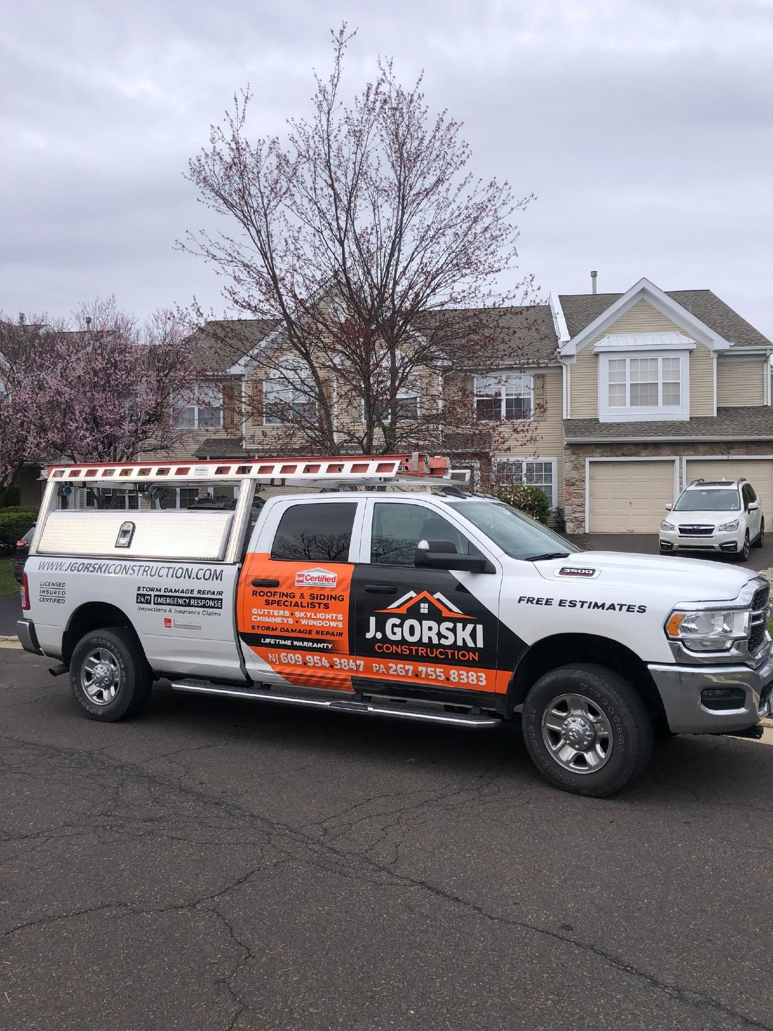 White work truck with company branding parked on a street in front of a house on a cloudy day.
