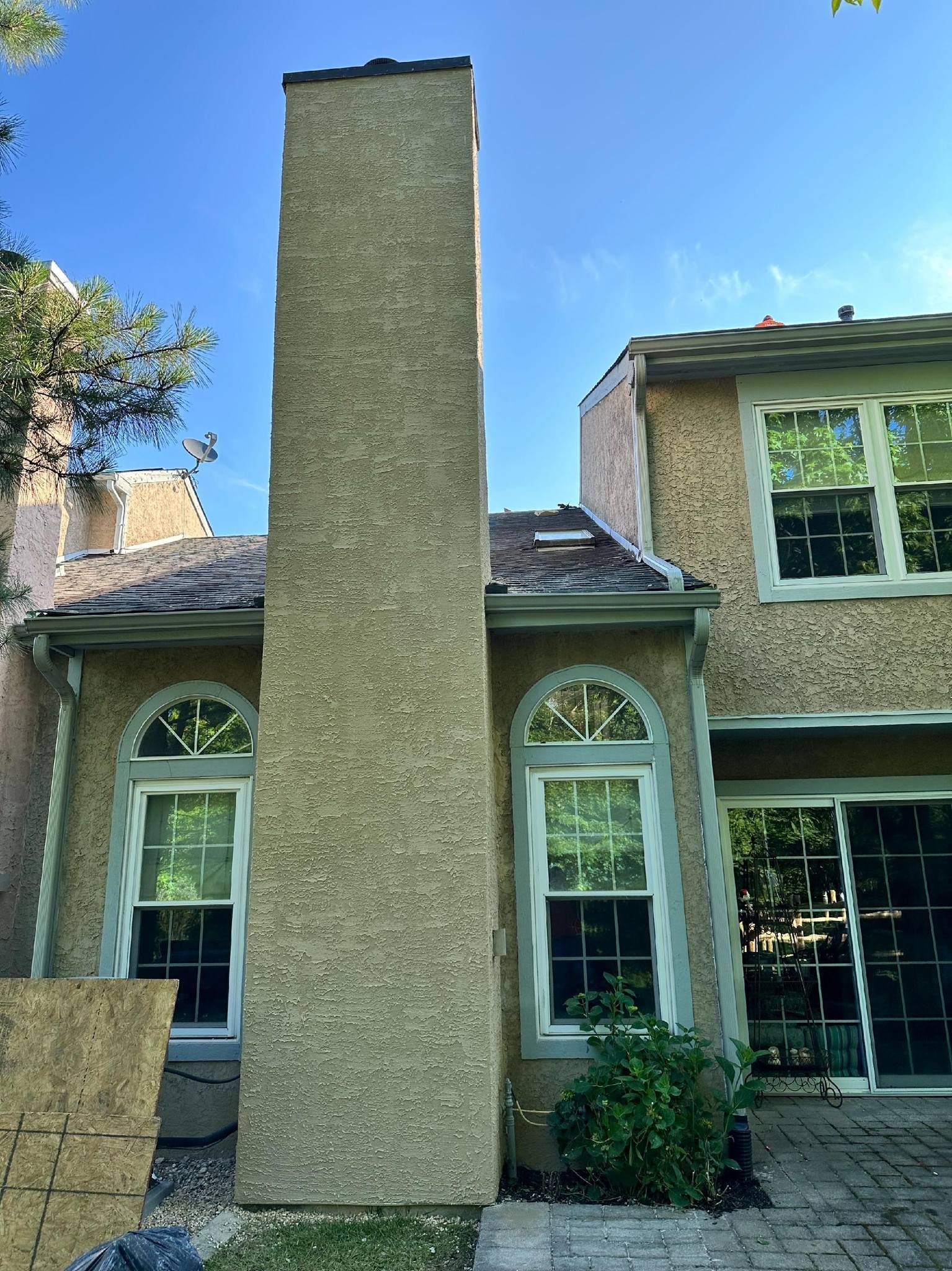 Tall beige chimney between a house with windows and a blue sky background.