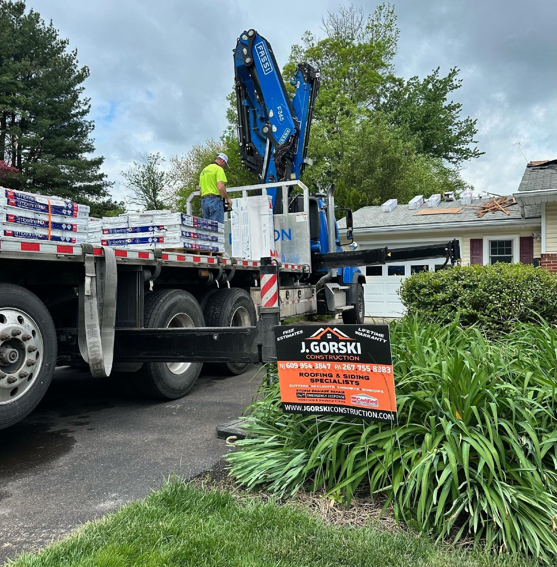 Roofing crew using a crane to lift shingles onto a house. A truck with 