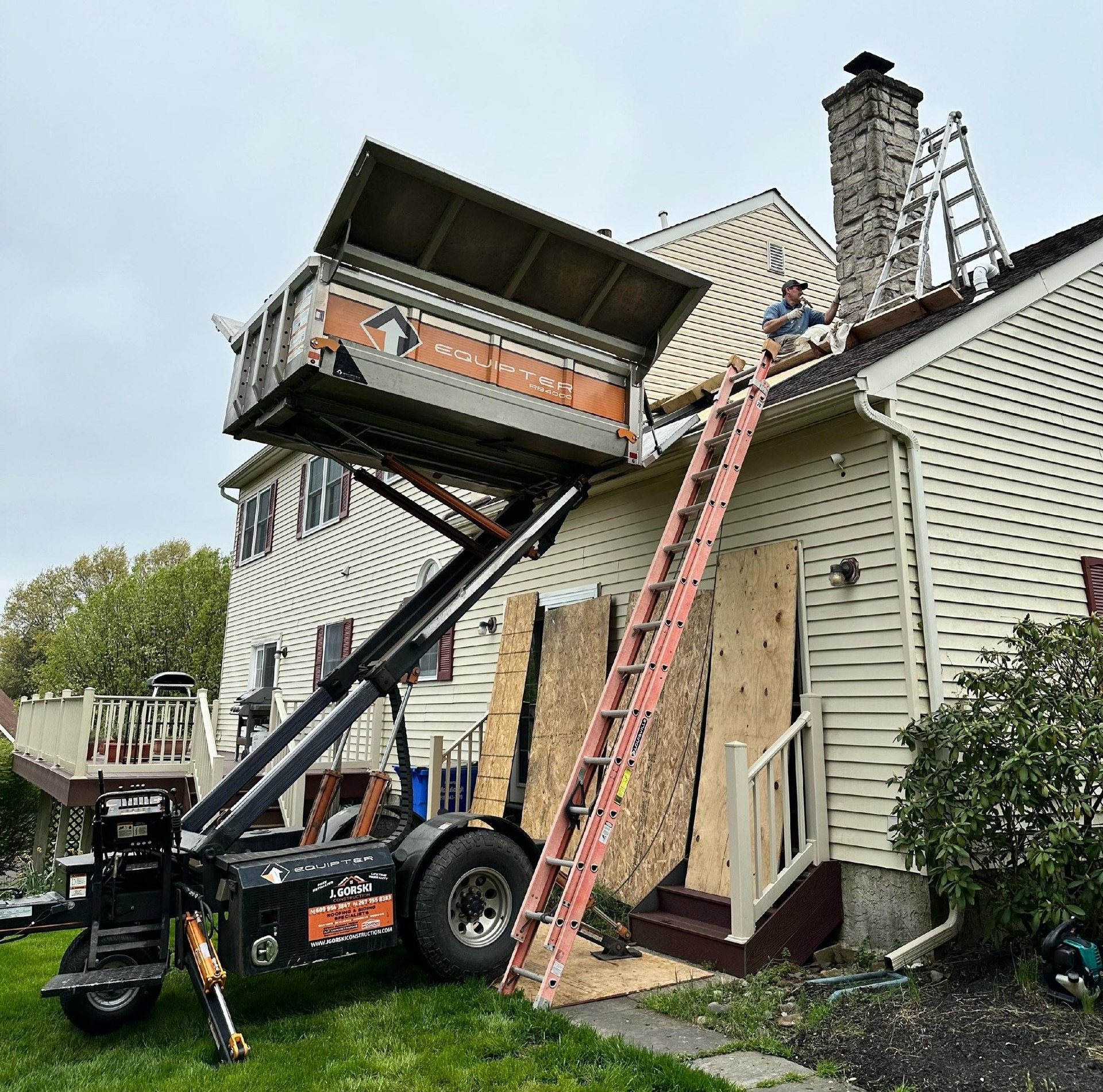 Construction worker on a roof near a lift removing debris. A ladder is leaning against the roof.