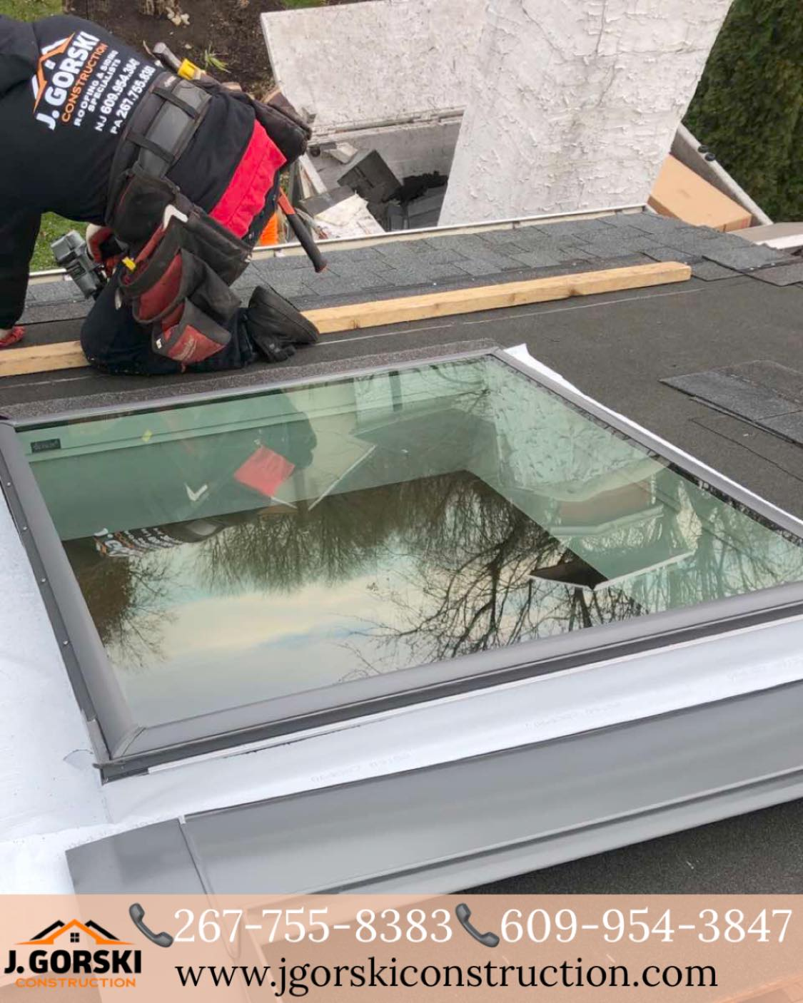 Roofer installs a skylight on a flat roof. The reflection of trees is visible in the glass.