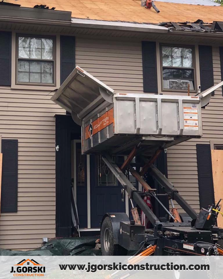 House with roofing work in progress; a worker on the roof, lift in front of the door.