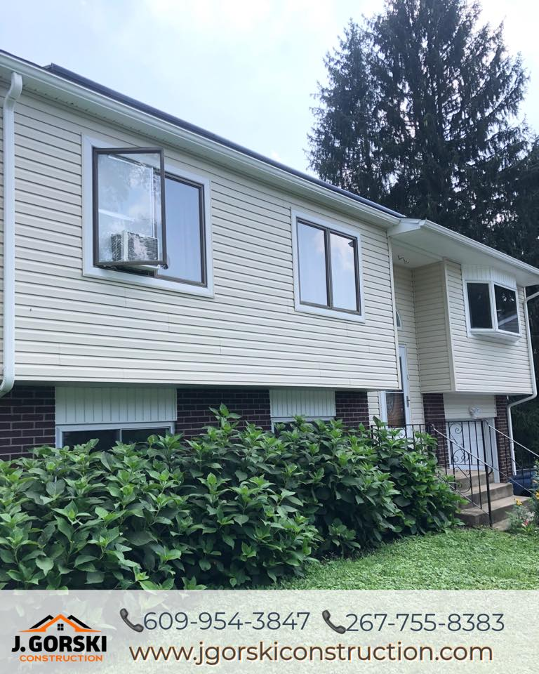 Beige-sided house with dark trim and windows. Green shrubs in front. J. Gorski Construction contact info at bottom.