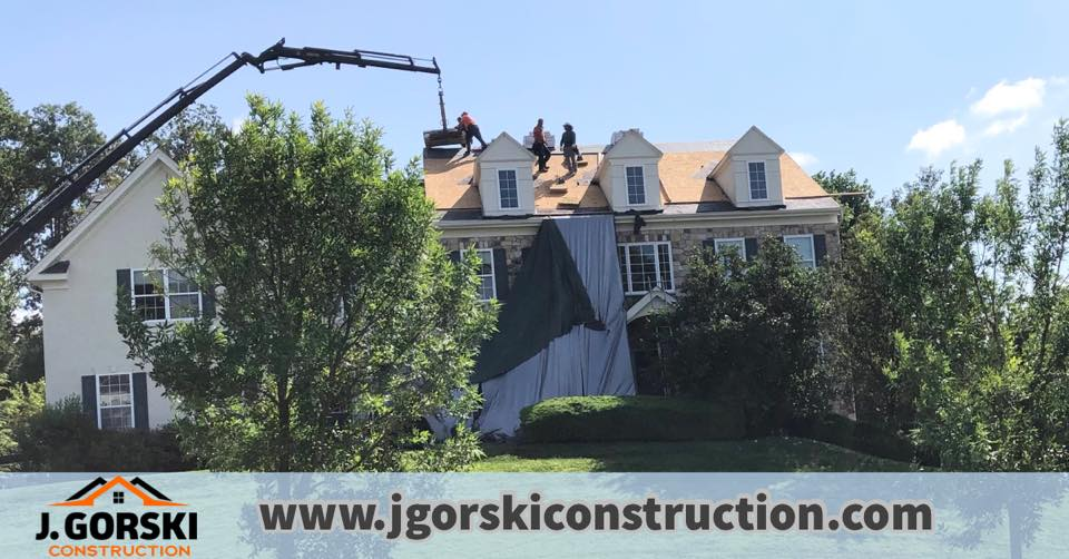 Roofers working on a house roof with a crane; green trees and a sunny sky.
