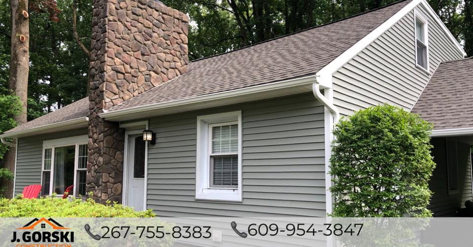 House with stone chimney, green siding, brown roof, and white window frames.