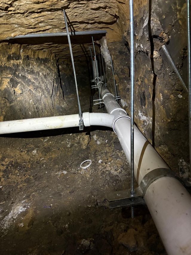 Copper pipes with a silver valve, connected with brass fittings, against a beige wall.