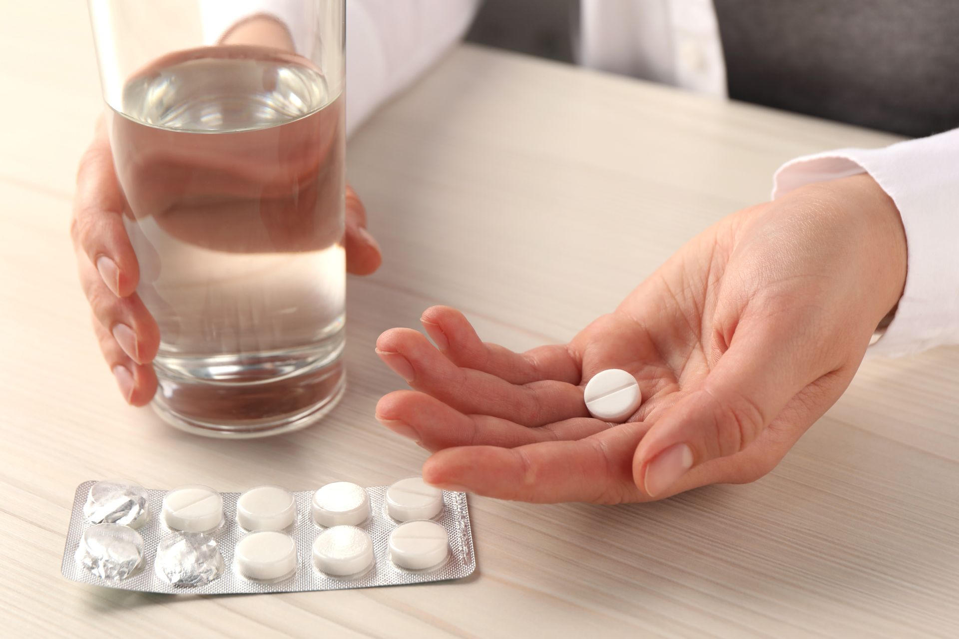 A person is holding a glass of water and a blister pack of pills.