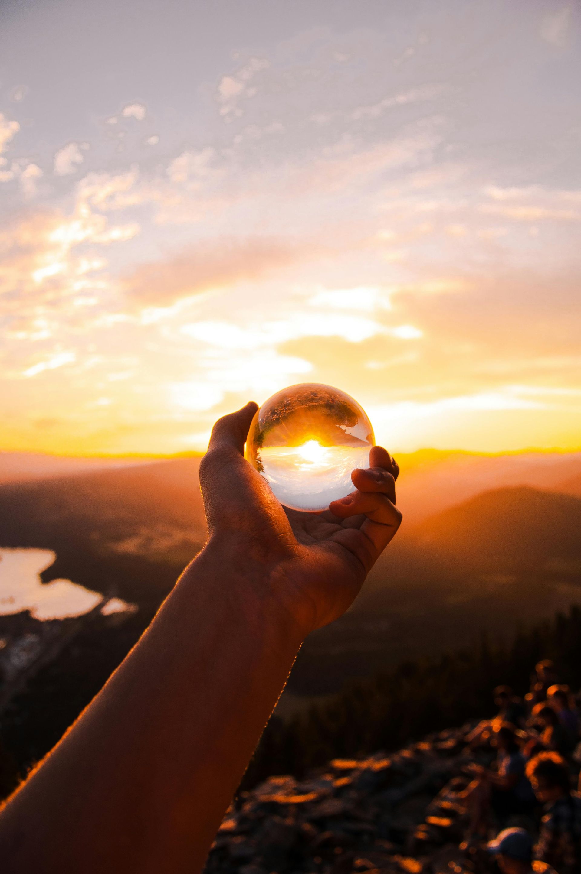 A person is holding a glass ball in front of a sunset.