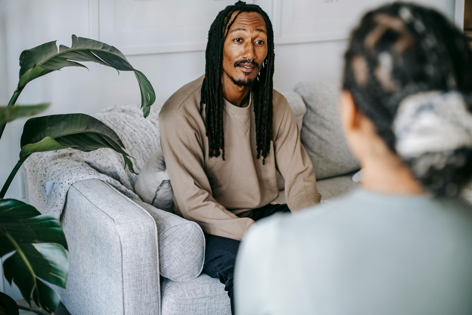A man with dreadlocks is sitting on a couch talking to a woman.