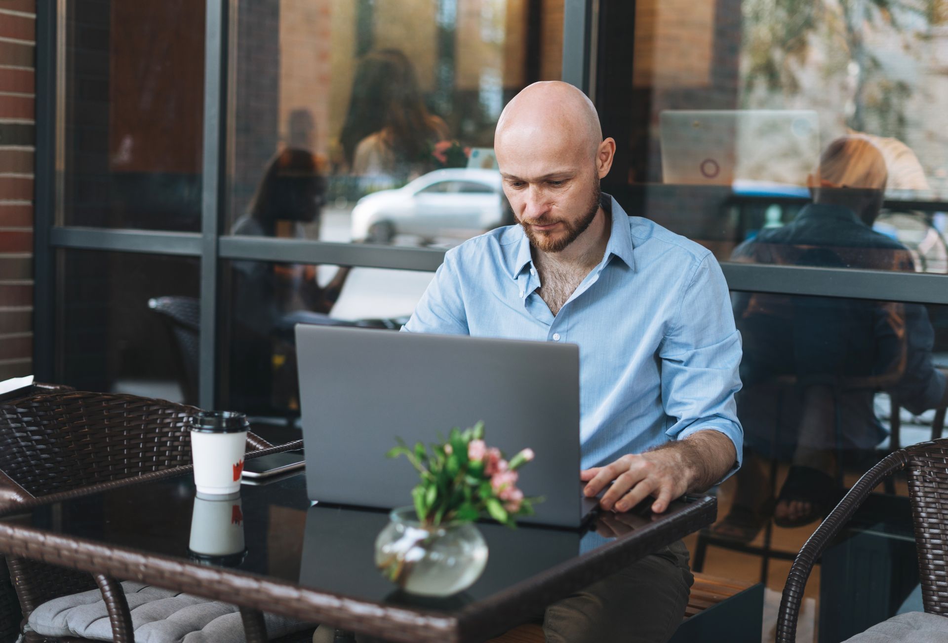 Bald man working on laptop at outdoor cafe table.